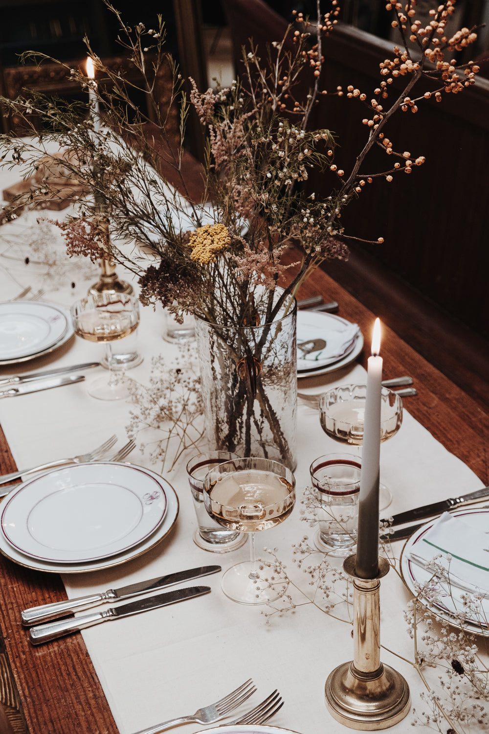 Elegant, classical table setting in the warehouse of Wildschut Antiques, featuring antique porcelain plates with an “M” monogram, vintage silver-plated cutlery by Sola, and a crisp white linen tablecloth. Accented with champagne coupes, antique water glasses, brass candle holders with a flickering candles, and a touch of florals.