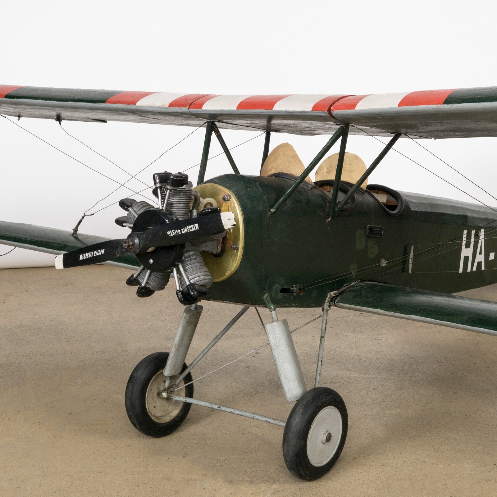 Close-up of the engine of a dark green vintage biplane model—a finely crafted 1970s replica of the 1954 Ha-Pao aircraft—featuring bold red and white striped wings. Available at Wildschut Antiques.