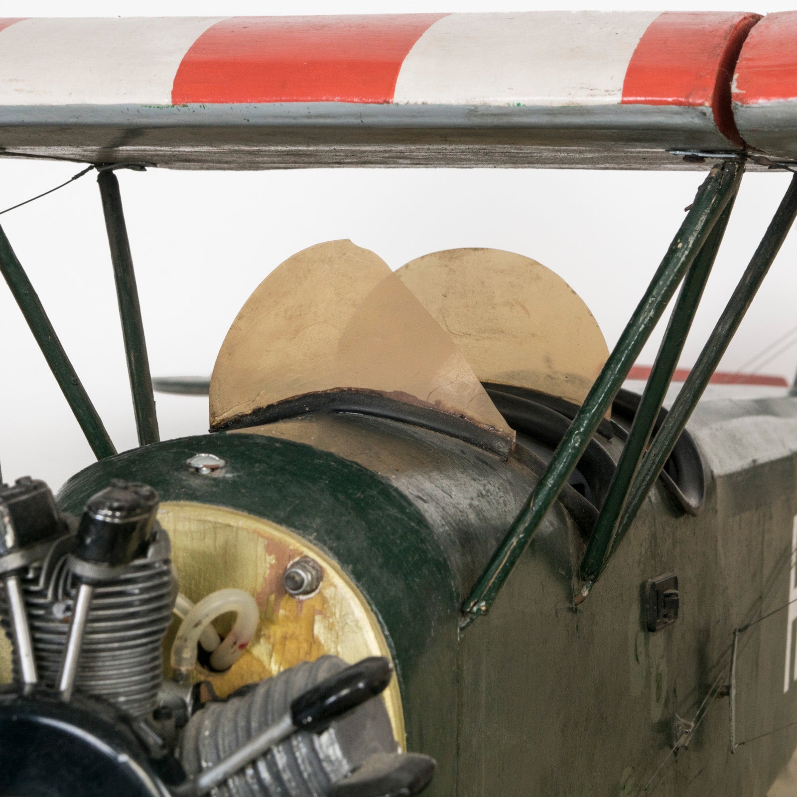 Close-up of the engine and cockpit of a dark green vintage biplane model—a finely crafted 1970s replica of the 1954 Ha-Pao aircraft—featuring bold red and white striped wings. Available at Wildschut Antiques.