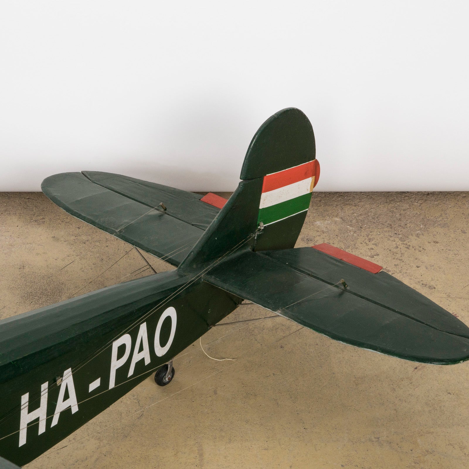 Close-up of the tail of a dark green vintage biplane model—a finely crafted 1970s replica of the 1954 Ha-Pao aircraft—featuring bold red and white striped wings. Available at Wildschut Antiques.