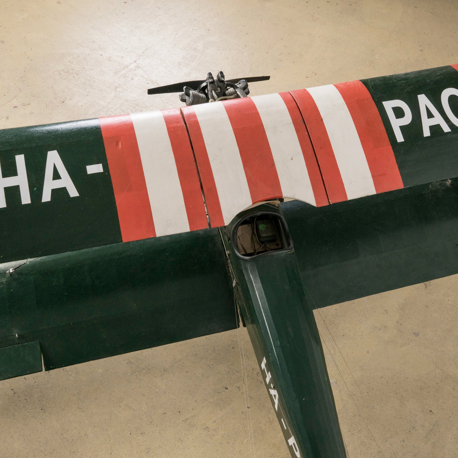 Close-up of the wings of a dark green vintage biplane model—a finely crafted 1970s replica of the 1954 Ha-Pao aircraft—featuring bold red and white striped wings. Available at Wildschut Antiques.