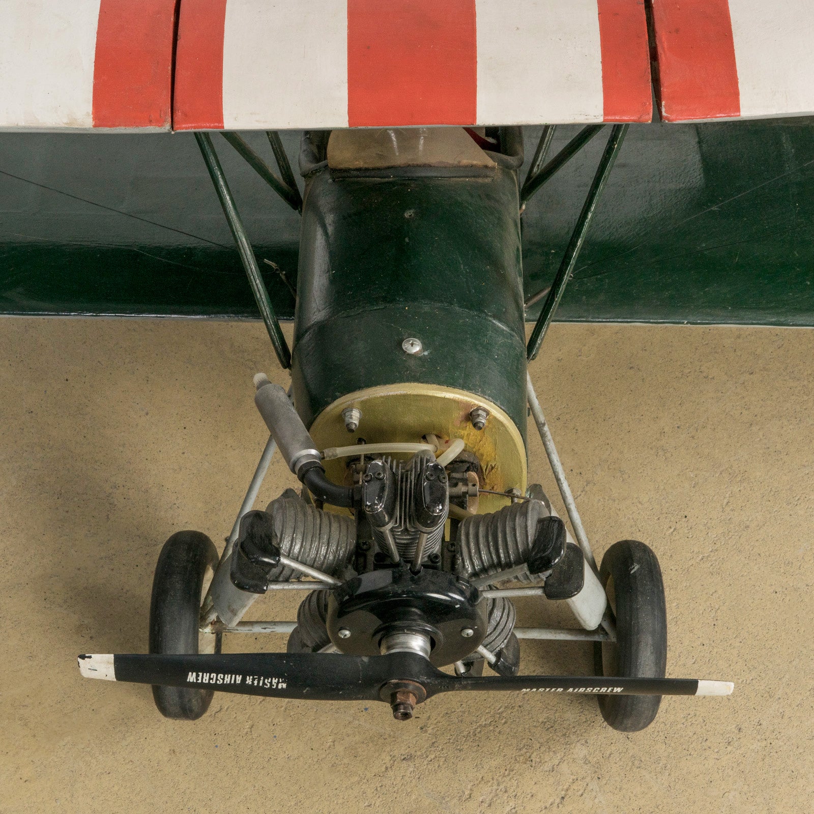 Close-up of the engine of a dark green vintage biplane model—a finely crafted 1970s replica of the 1954 Ha-Pao aircraft—featuring bold red and white striped wings. Available at Wildschut Antiques.