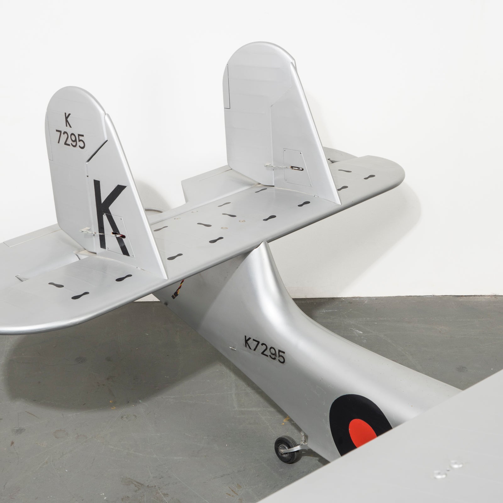 Close-up of the tail of a large vintage model of a World War I-era airplane with a silver finish, black and red detailing, and a large 'K' on the tail wing