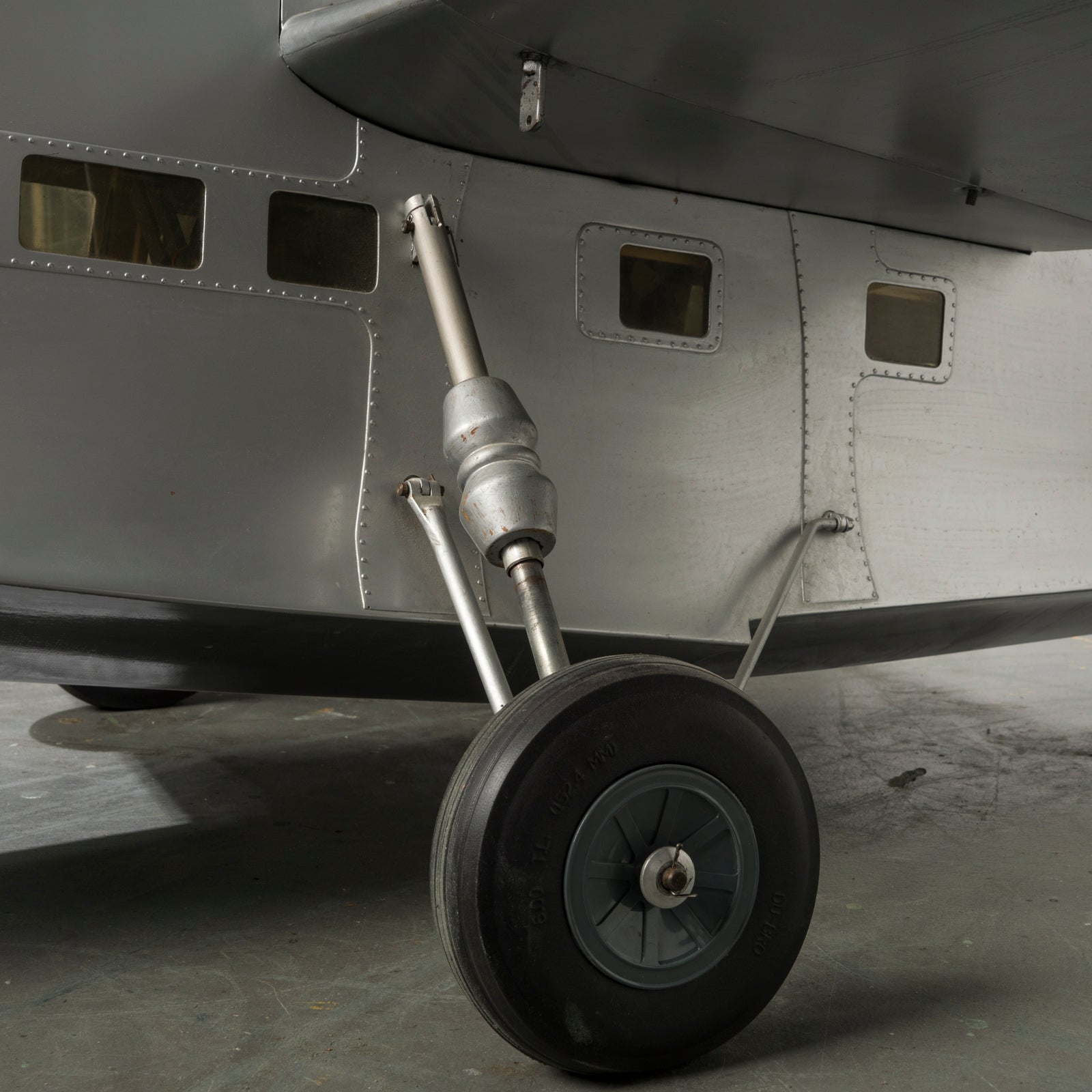 Close-up of the side, one wheel, and a part of the wing of a large vintage model of a World War I-era airplane with a silver finish