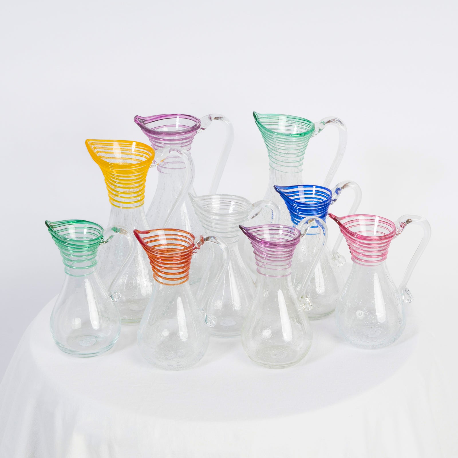 Collection of hand-blown clear glass pitchers with bubble texture and colorful swirls at the top, for serving or use as vases, available at Wildschut Antiques