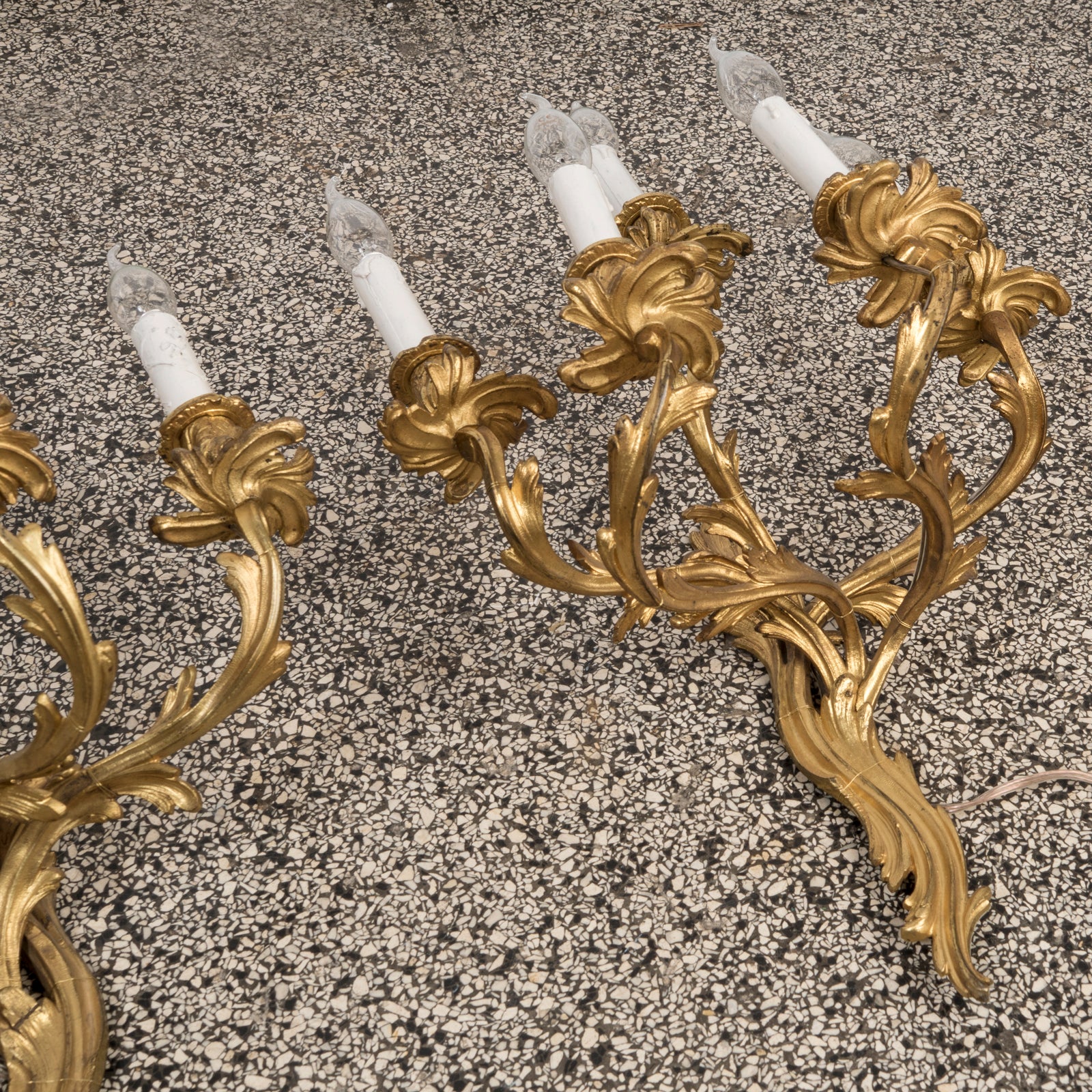 Close-up of a pair of grand 19th-century French Rococo five-light sconces in opulent gilded bronze, resting on a terrazzo floor.