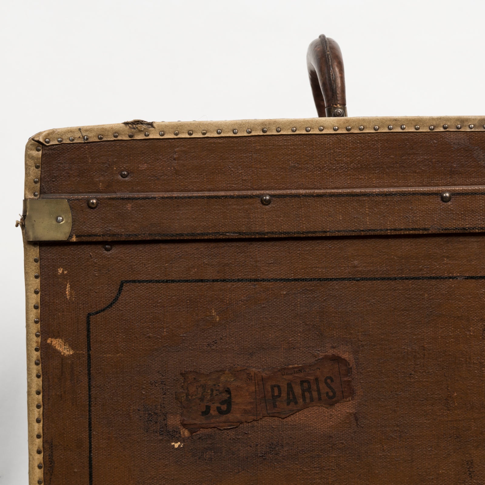 Close-up of a brown vintage canvas cube-shaped trunk with a leather handle and metal accents and a Paris label on the side
