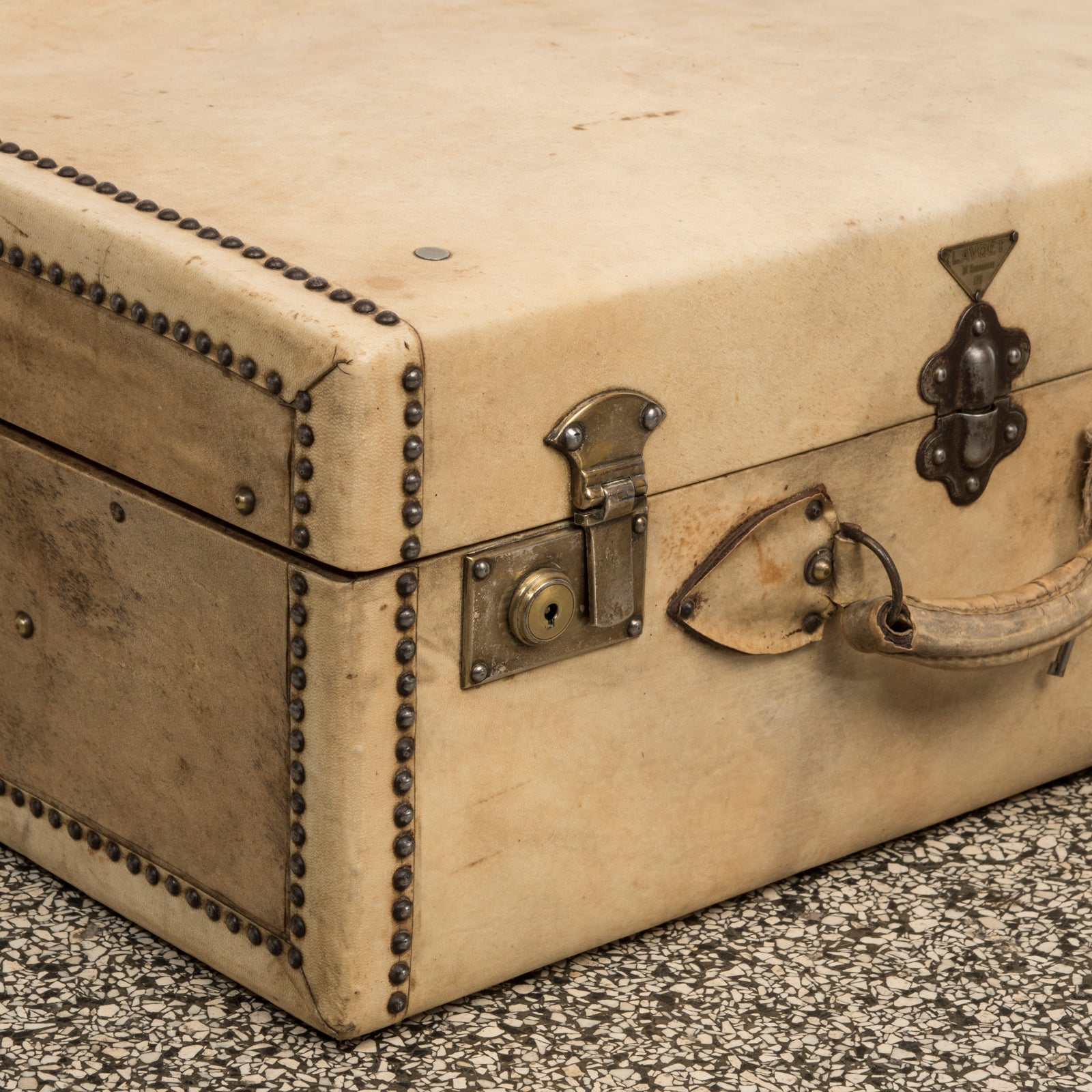 Close-up of a vintage French cream leather suitcase with brass studs, leather handle, and a lock plate by Lavoet, available at Wildschut Antiques