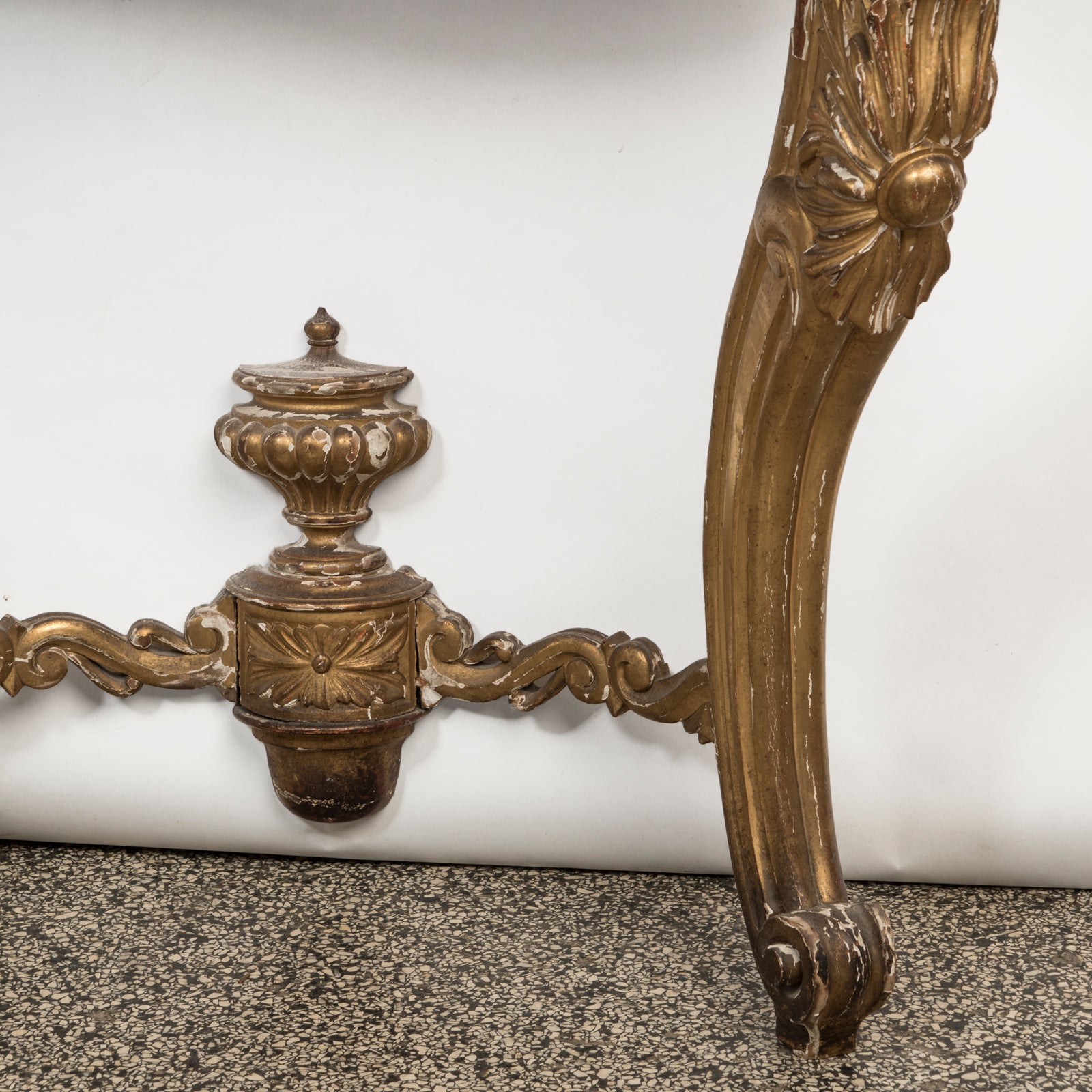 Close-up of a highly decorative antique French Louis XV style gilt wood console table with a white marble top, featuring intricate gilded designs and resting on carved legs. Showing some age appropriate wear and original patina.