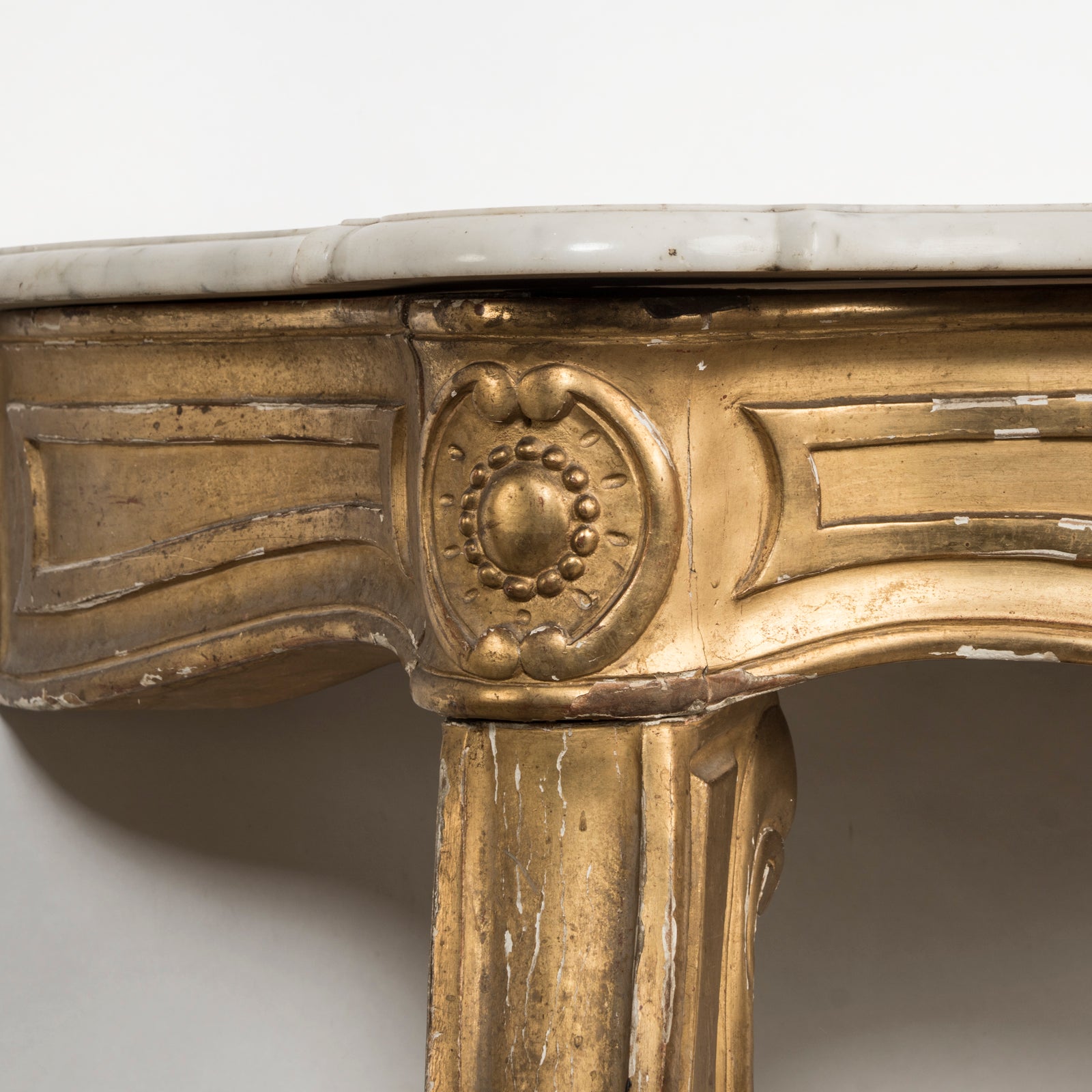 Close-up of a highly decorative antique French Louis XV style gilt wood console table with a white marble top, featuring intricate gilded designs and resting on carved legs. Showing some age appropriate wear and original patina.