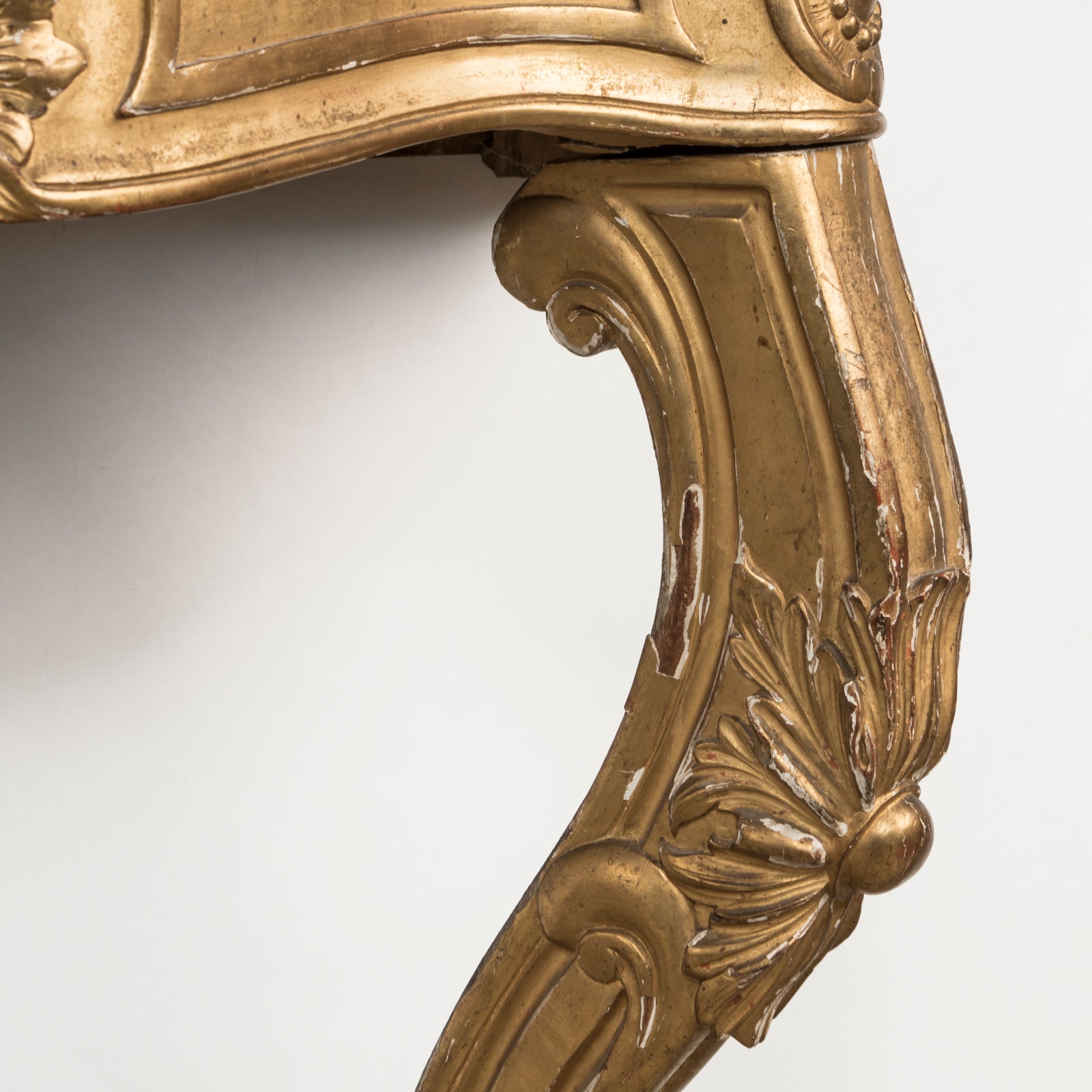 Close-up of a highly decorative antique French Louis XV style gilt wood console table with a white marble top, featuring intricate gilded designs and resting on carved legs. Showing some age appropriate wear and original patina.