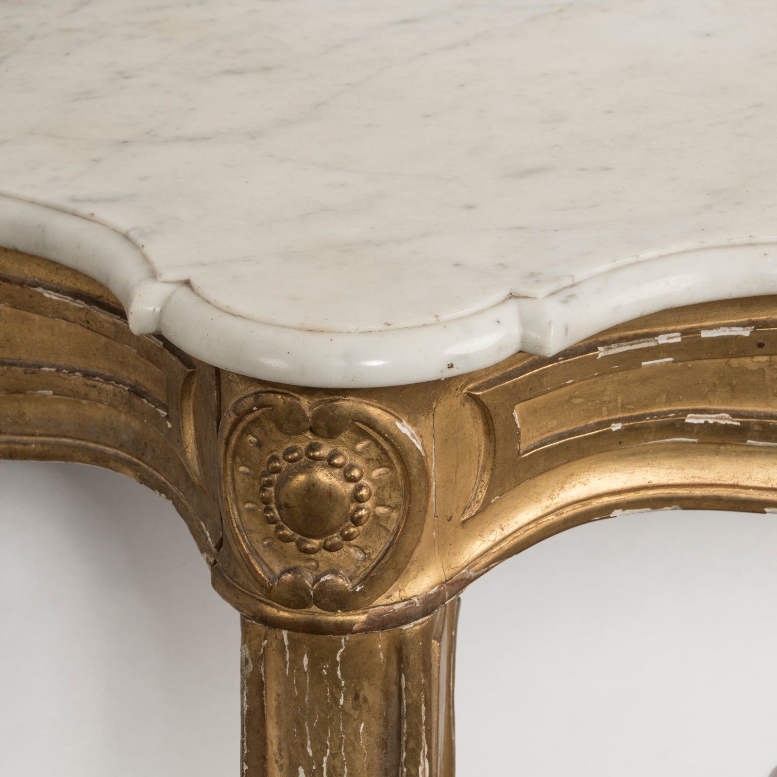 Close-up of a highly decorative antique French Louis XV style gilt wood console table with a white marble top, featuring intricate gilded designs and resting on carved legs. Showing some age appropriate wear and original patina.