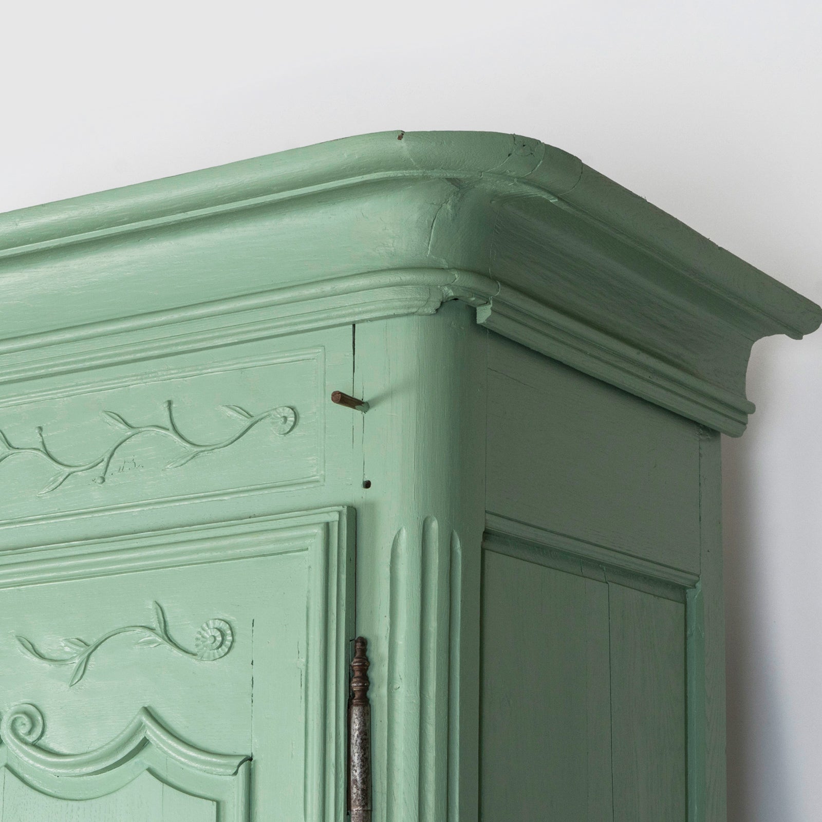 Close-up of the top of a 19th-century green French marriage armoire with carved foliage motifs from Wildschut Antiques
