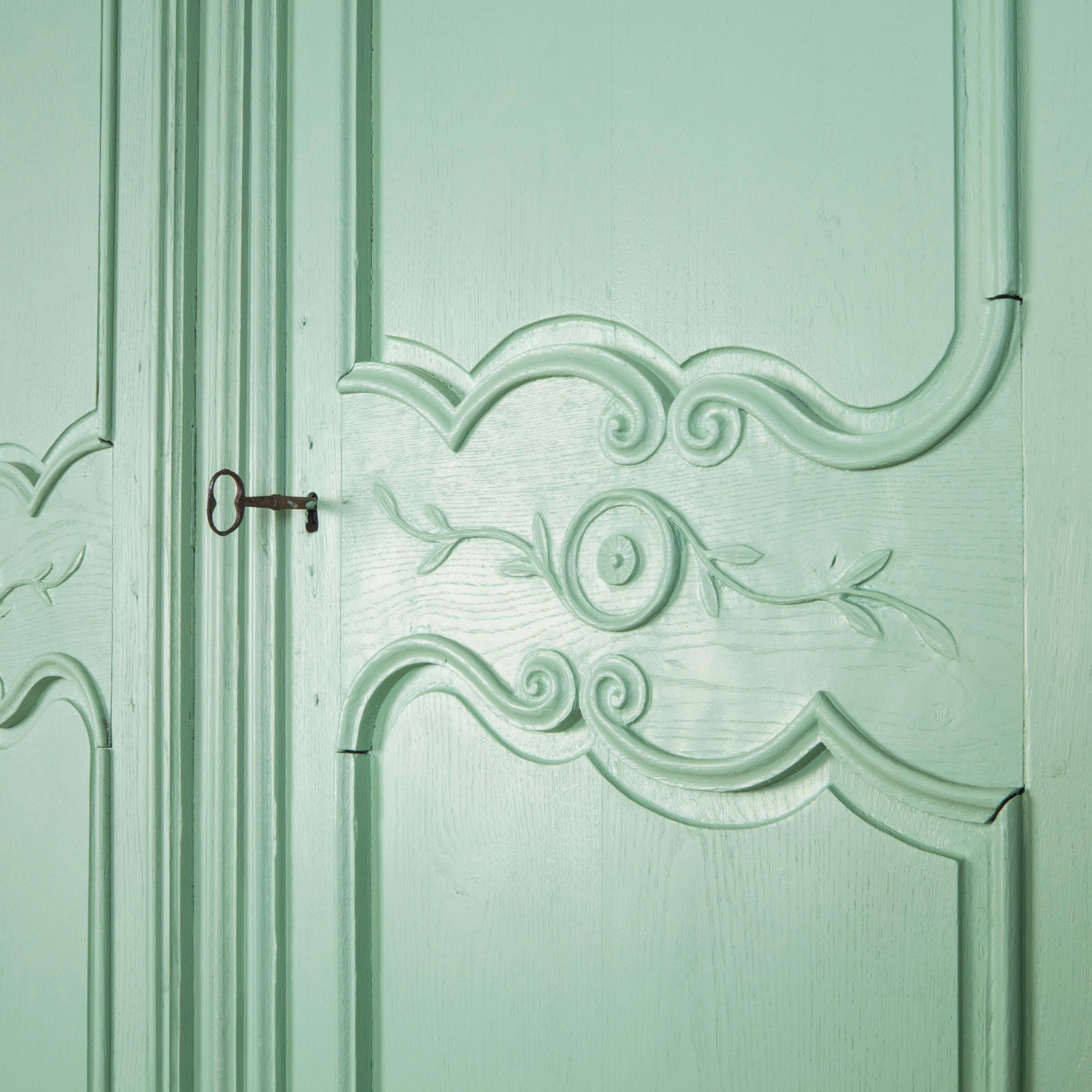 Close-up of a door of a soft green painted French marriage armoire from the 19th century with carved foliage motifs, available at Wildschut Antiques
