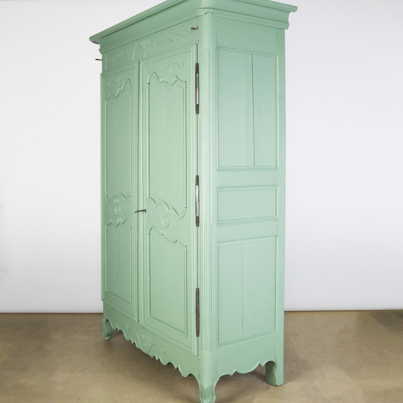 Side view of a soft green painted French marriage armoire from the 19th century with carved foliage motifs and steel barrel hinges, available at Wildschut Antiques