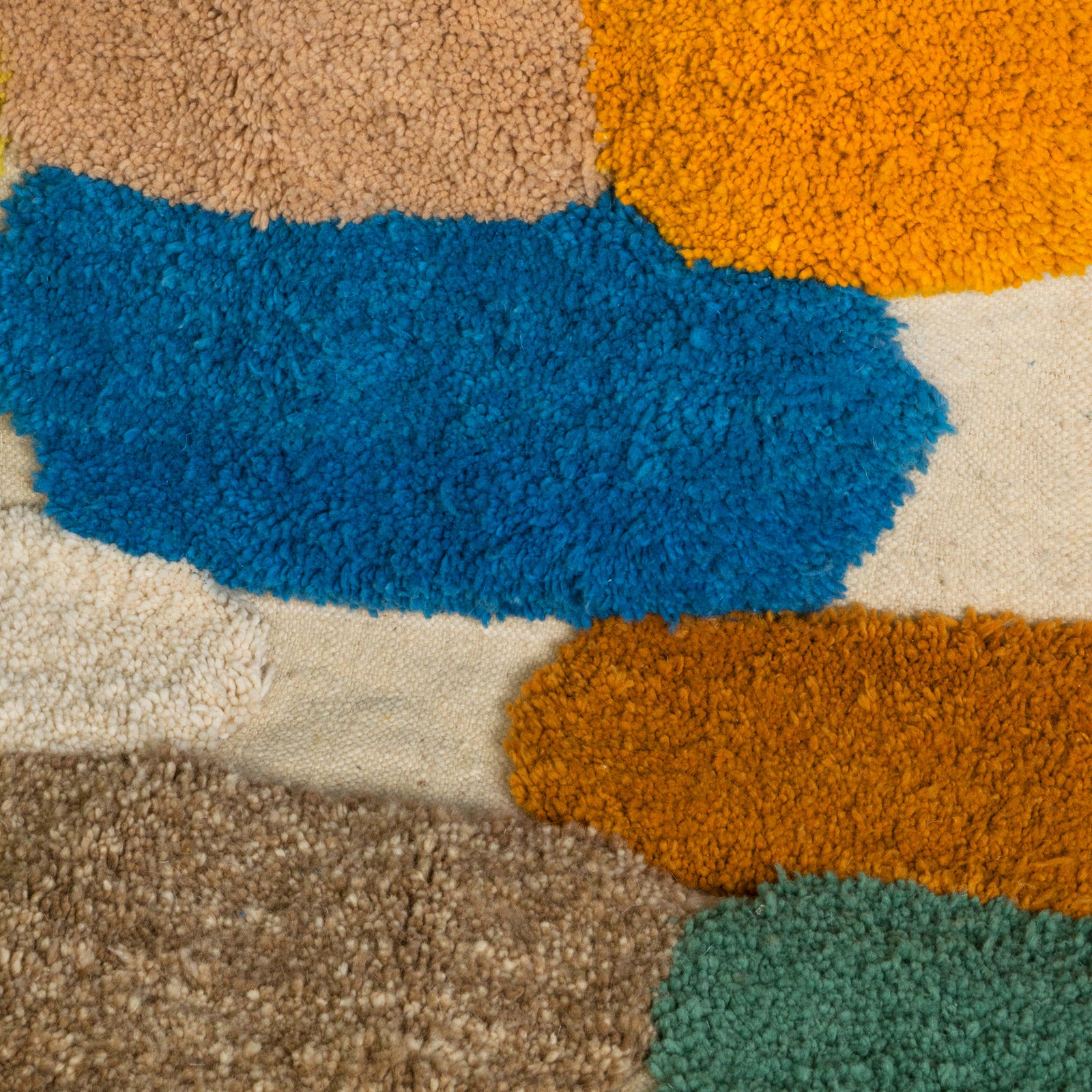 Close-up of a vintage 1970s Moroccan rug featuring an abstract composition of vibrant, irregularly shaped tufts in bold colors—such as cobalt blue, mustard yellow, fuchsia, burnt orange, and olive green—set against a natural cream background. The rug has a playful, textured appearance and is finished with fringed tassels on both ends.