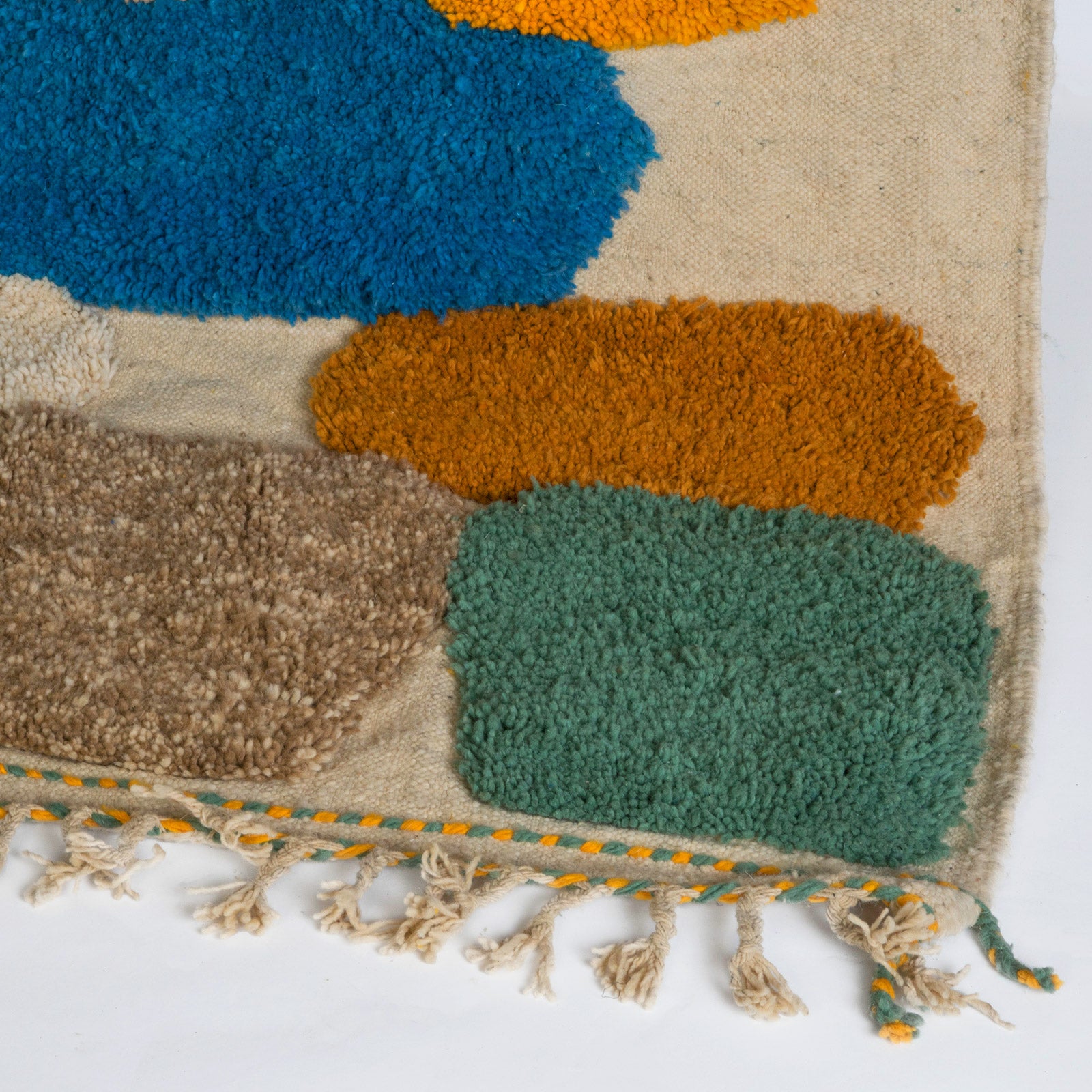 Close-up of a vintage 1970s Moroccan rug featuring an abstract composition of vibrant, irregularly shaped tufts in bold colors—such as cobalt blue, mustard yellow, fuchsia, burnt orange, and olive green—set against a natural cream background. The rug has a playful, textured appearance and is finished with fringed tassels on both ends.