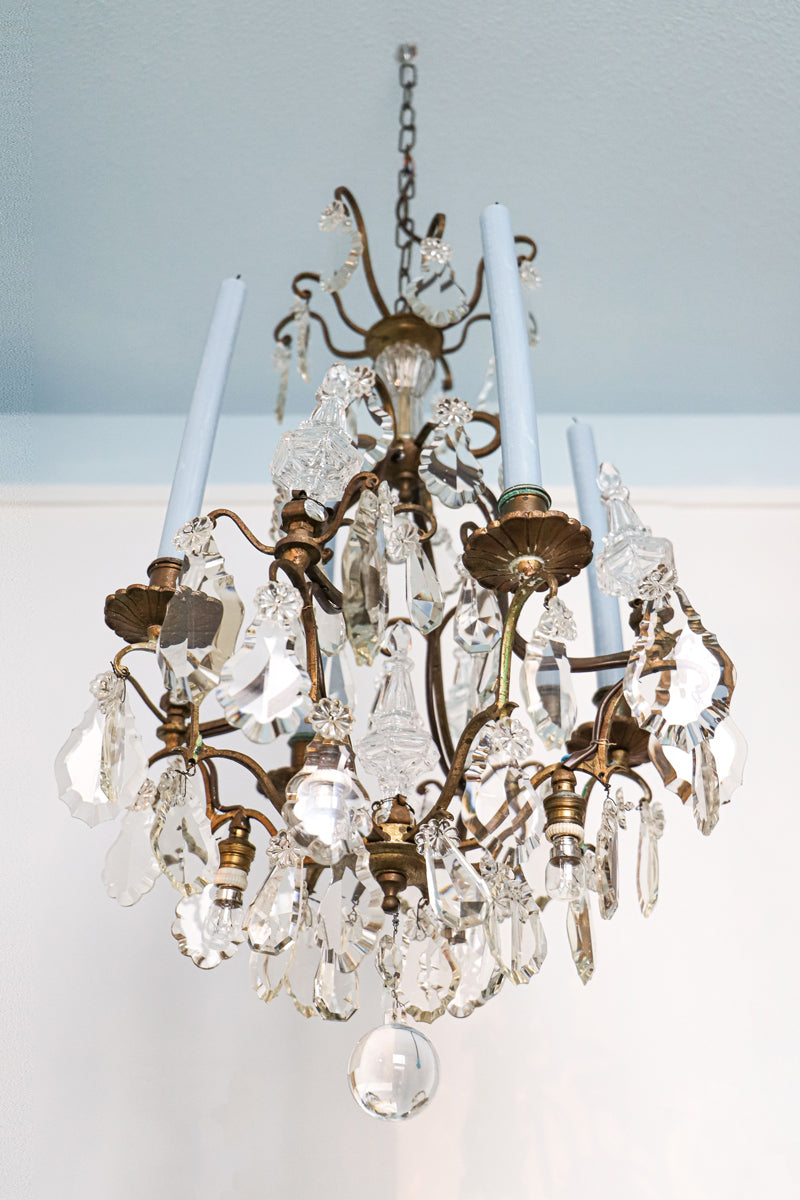 Antique French crystal chandelier with candle holders and four light blue candles, suspended from a matching light blue ceiling.