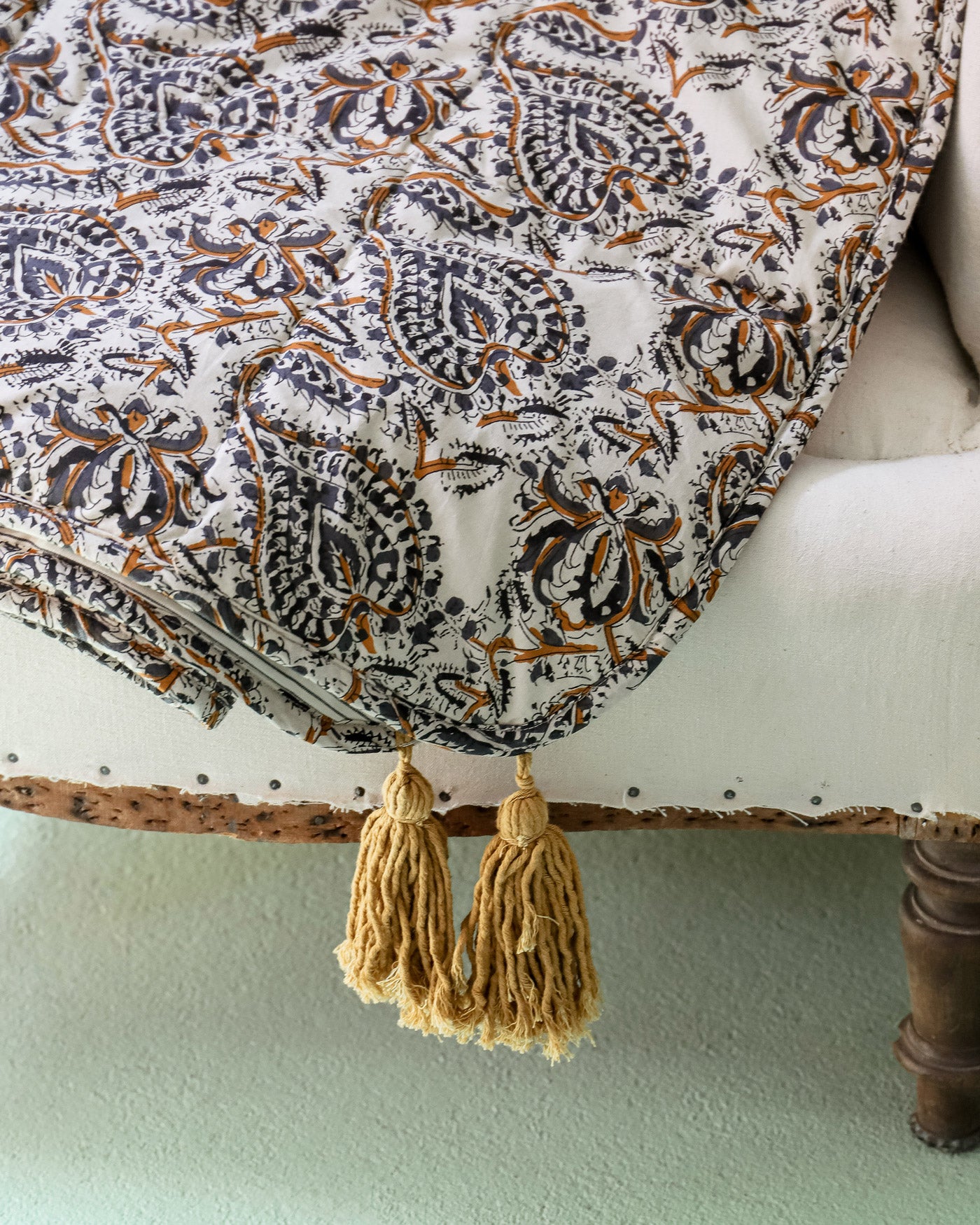 Close-up of a cotton blanket with a paisley pattern and two yellow tassels, elegantly draped over an antique chair.