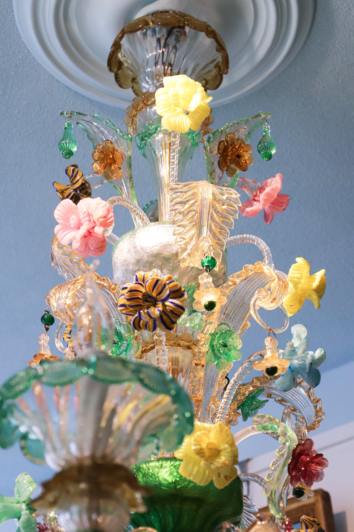 Close-up of the top part of a vibrant vintage green Venetian Murano glass chandelier with floral patterns and multiple arms, each holding glass flower ornaments, available at Wildschut Antiques