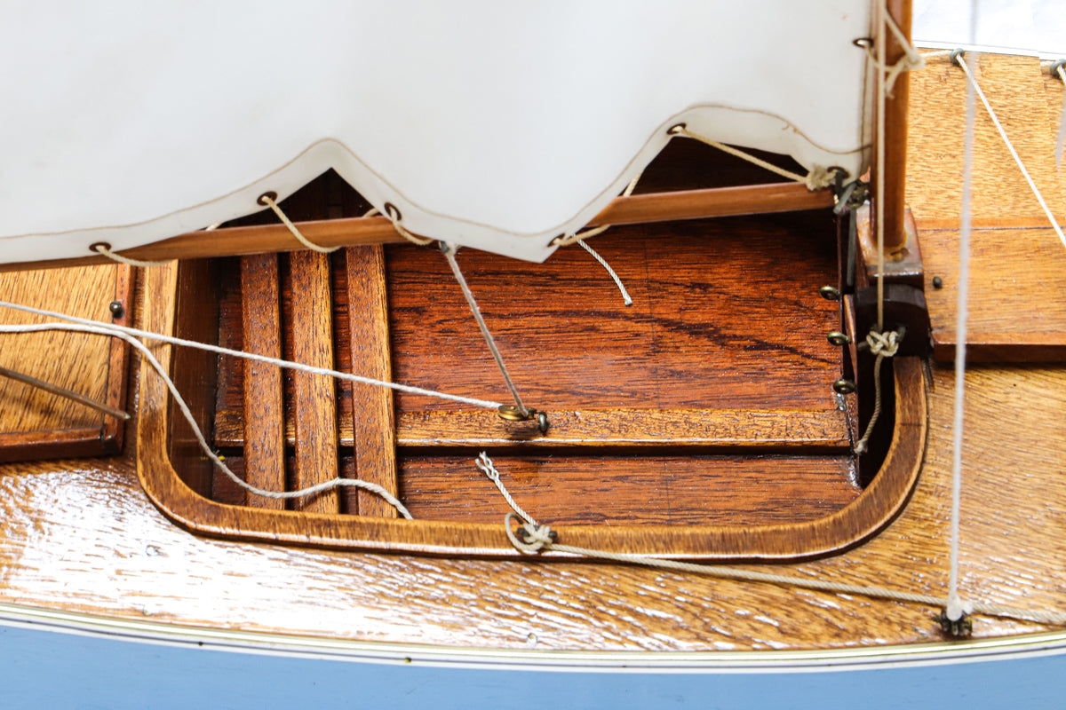 Close-up of a vintage blue and white sailboat model with a wooden structure and a white sail