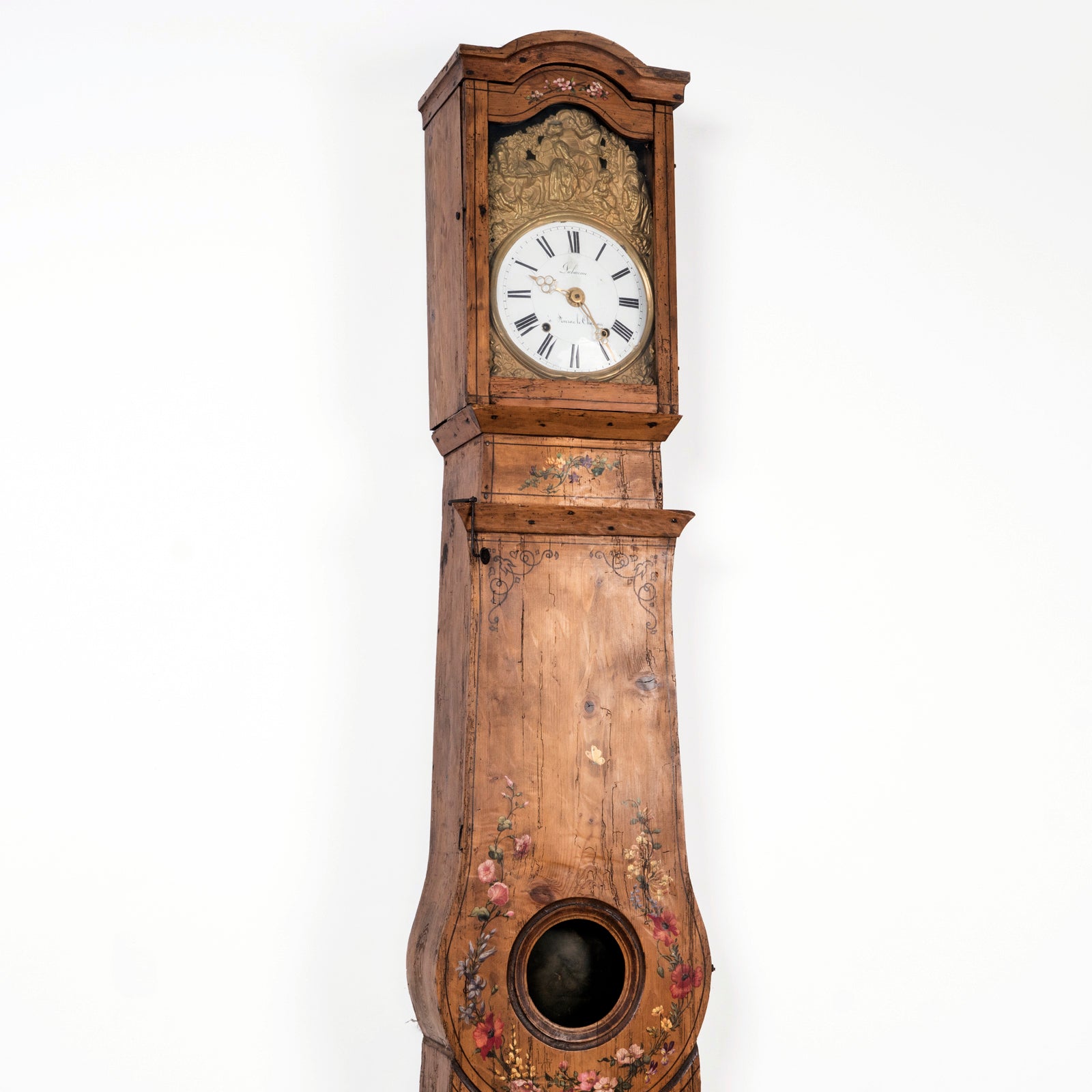 Close-up of the top part of a charming antique French tall case clock with a painted pine case decorated with floral motifs. Displayed against a clean background. Available at Wildschut Antiques.