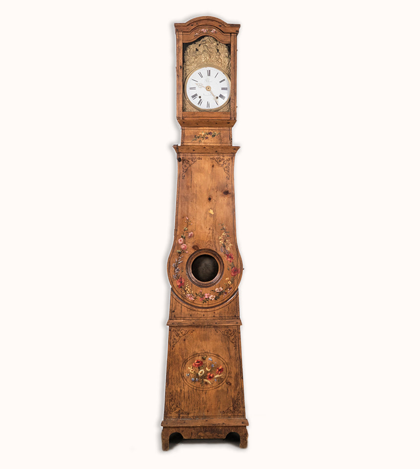 Charming antique French tall case clock with a painted pine case decorated with floral motifs. The porcelain dial is signed “Labaume, à Sévérac-le-Château” and set in an embossed frame, dating circa 1870. Displayed against a clean background. Available at Wildschut Antiques.