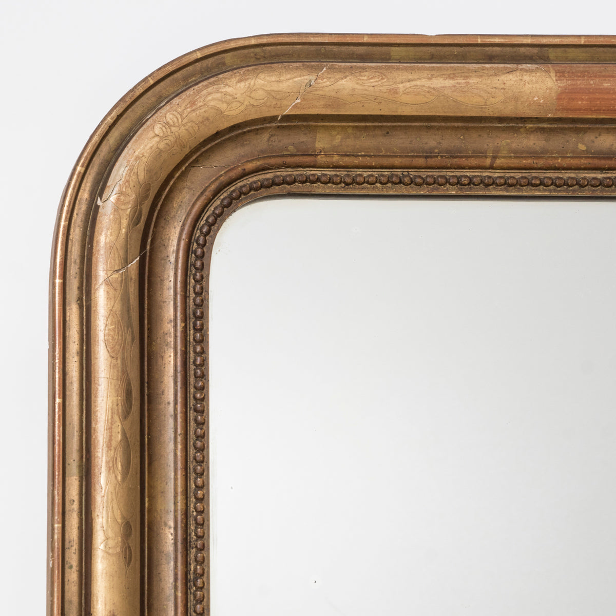 Close-up of an antique 19th-century French Louis Philippe-style gilt mirror, intricately etched with leaf and flower motifs and featuring an inner beaded border. Displayed against a clean background. Available at Wildschut Antiques.