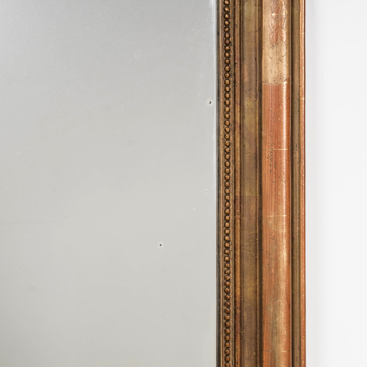 Close-up of an antique 19th-century French Louis Philippe-style gilt mirror, intricately etched with leaf and flower motifs and featuring an inner beaded border.