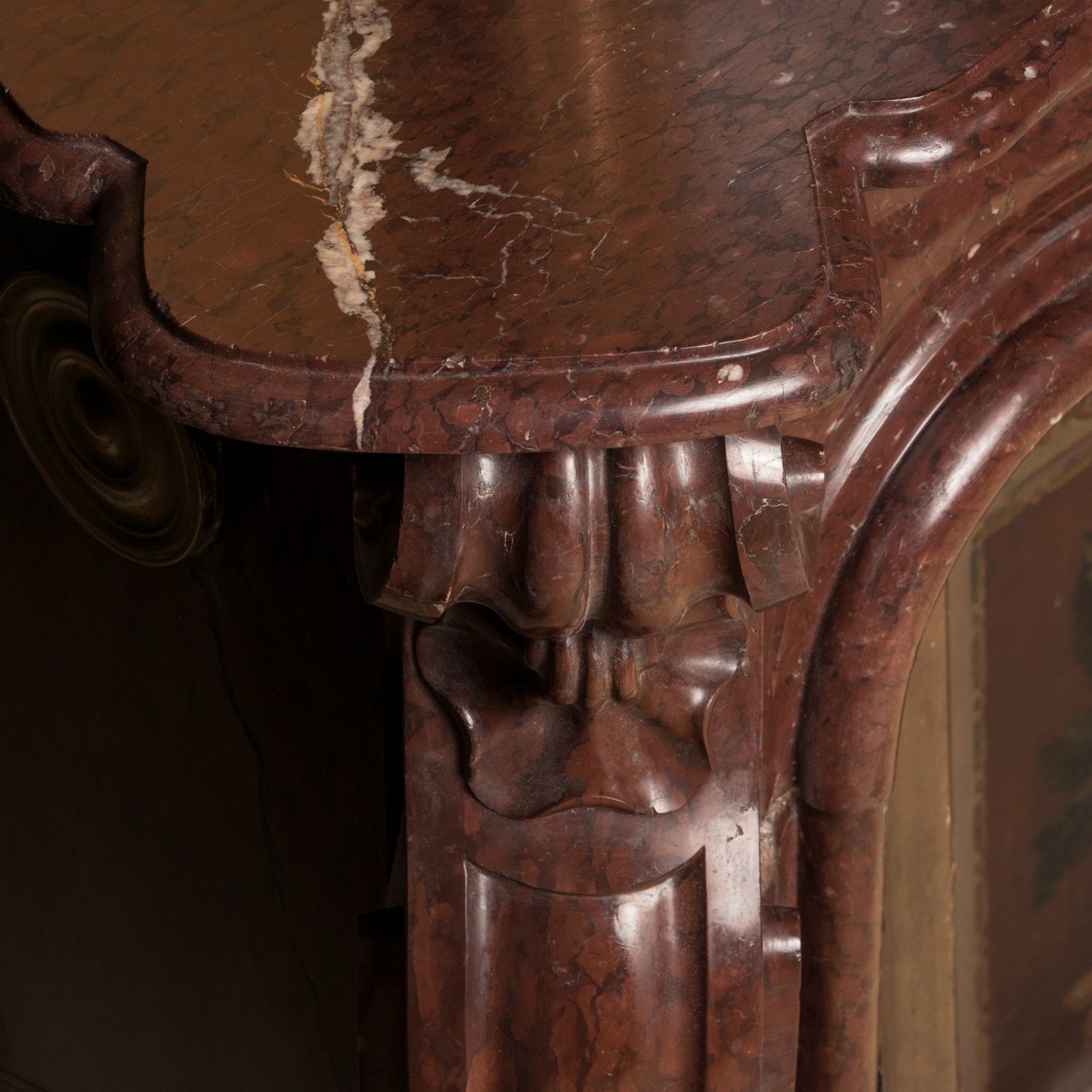 Close-up of a grand antique French Rococo Louis XV fireplace mantel, crafted from richly veined red-brown marble.