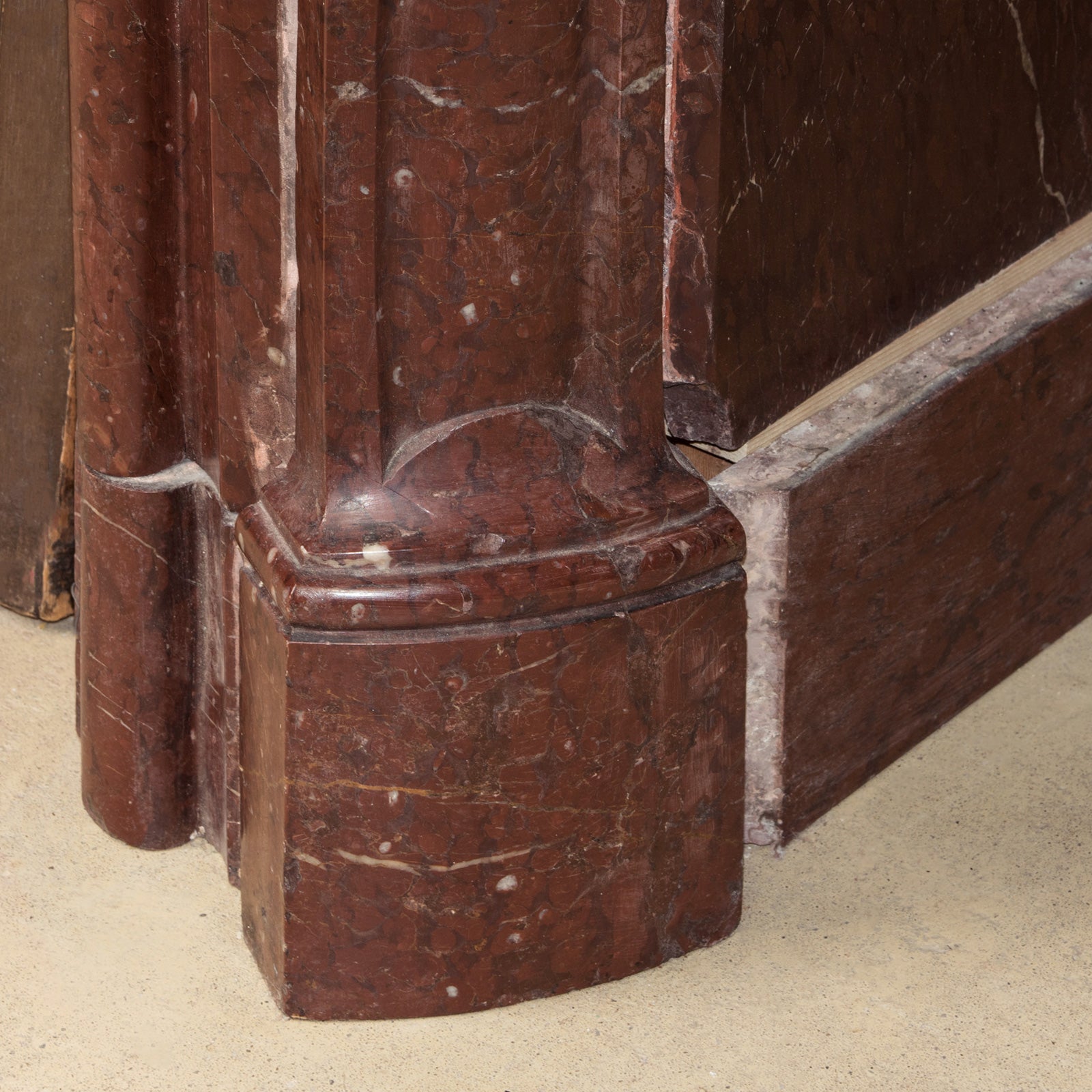 Close-up of a leg part of a grand antique French Rococo Louis XV fireplace mantel, crafted from richly veined red-brown marble.