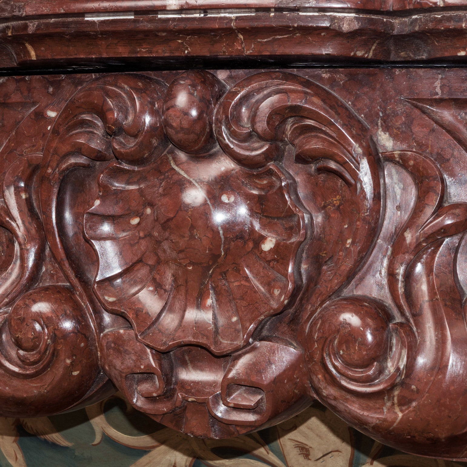 Close-up of a shell shape at the front of a grand antique French Rococo Louis XV fireplace mantel, crafted from richly veined red-brown marble.