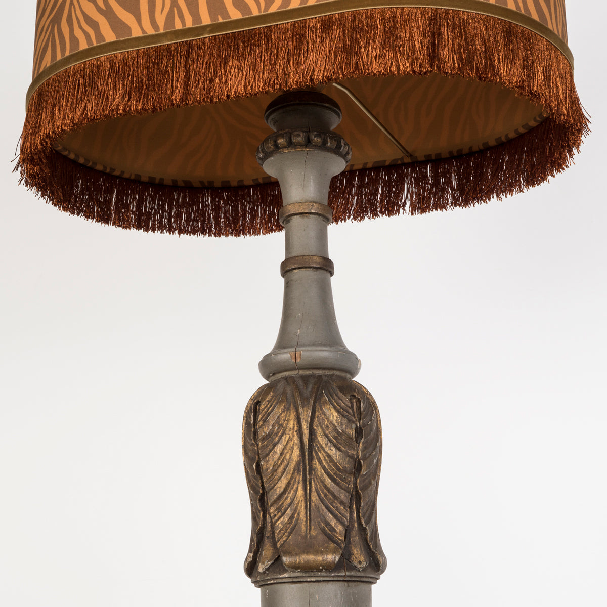 Close-up of an antique French Louis XVI-style standing lamp or pedestal, topped with an orange-brown lampshade by Dutch brand Palais, finished with orange fringes. Displayed against a clean background. Available at Wildschut Antiques.