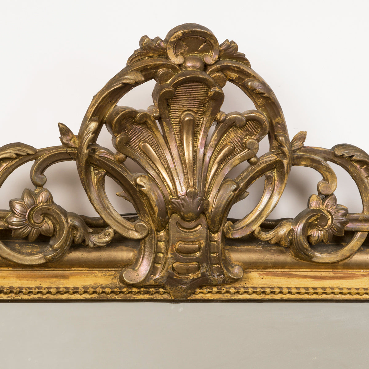 Close-up of the crest of an antique 19th-century French Louis Philippe-style gilt mirror featuring a decorative crest and pearl beading along the inner perimeter.