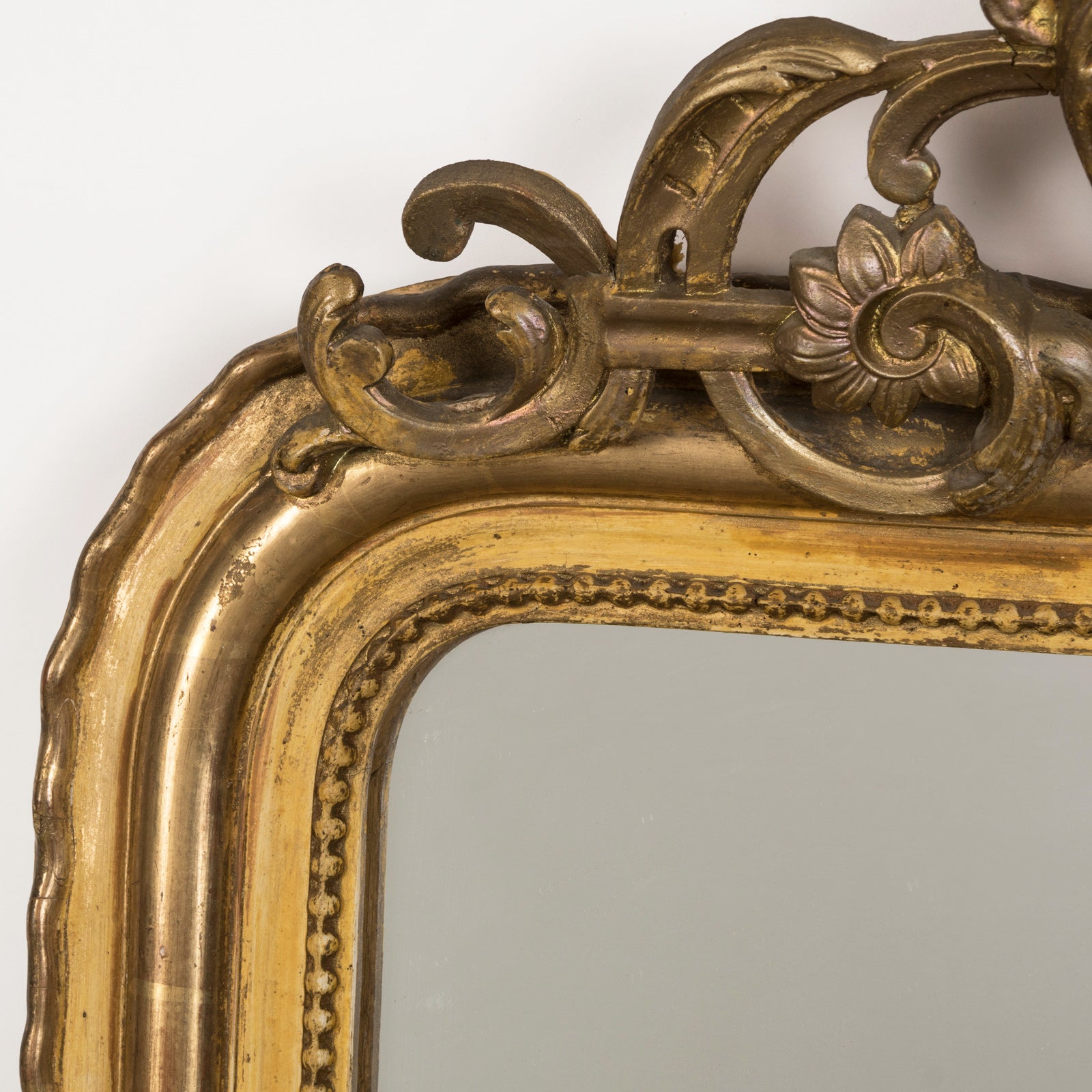 Close-up of an antique 19th-century French Louis Philippe-style gilt mirror featuring a decorative crest and pearl beading along the inner perimeter.