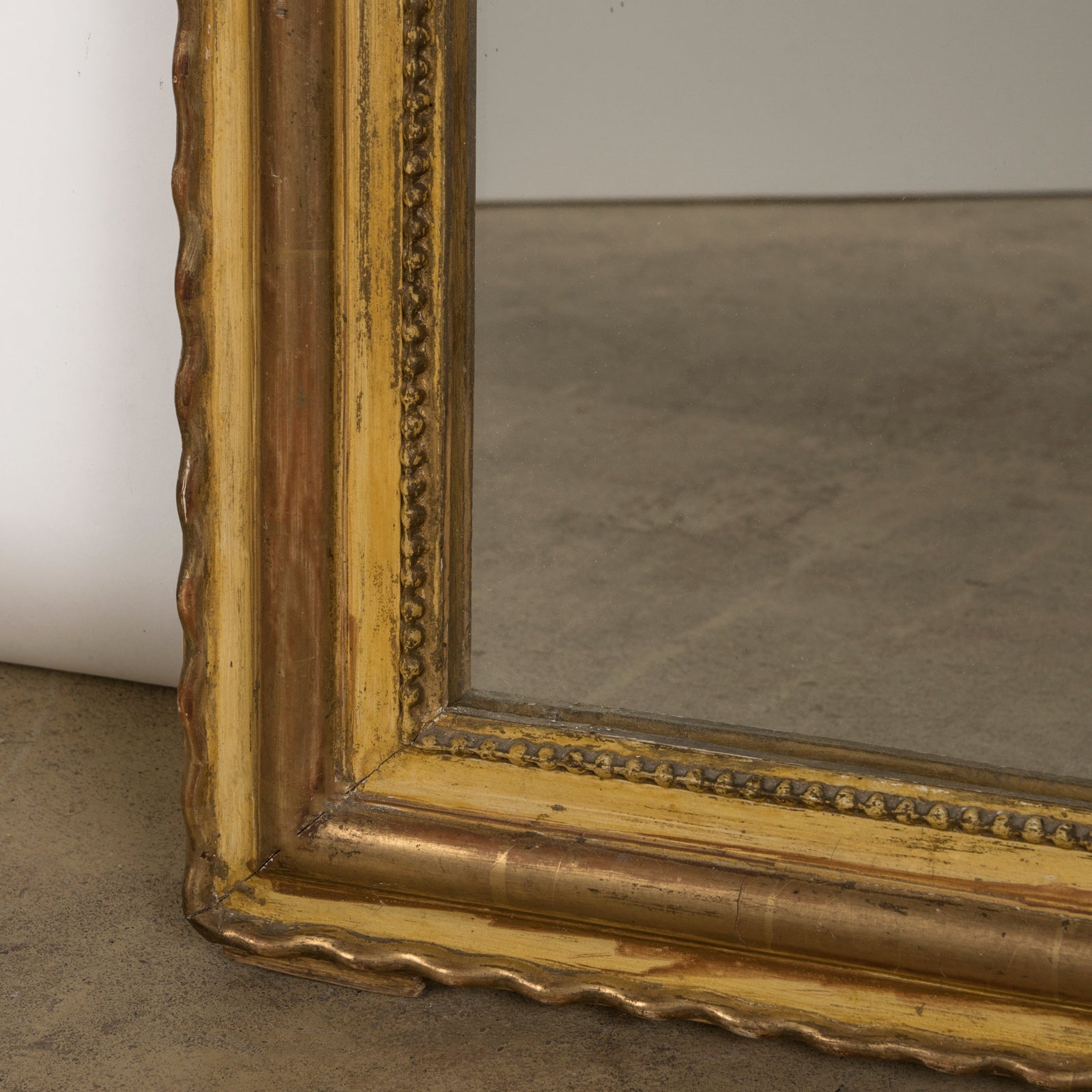 Close-up of an antique 19th-century French Louis Philippe-style gilt mirror featuring a decorative crest and pearl beading along the inner perimeter.