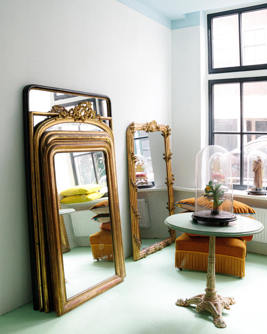 Interior of Wildschut Antiques featuring a stack of antique French mirrors on a mint green floor, alongside an antique French green bistro table.