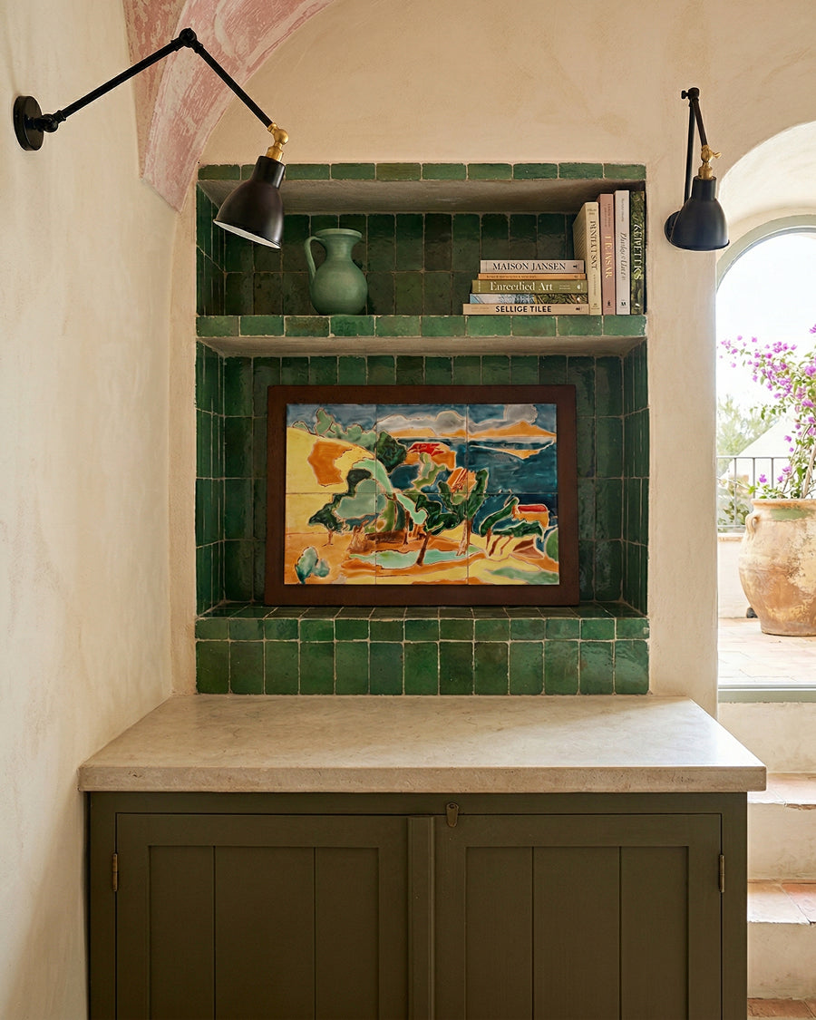Niche with green tiles, framed artwork, and books in a kitchen with a window and plant.
