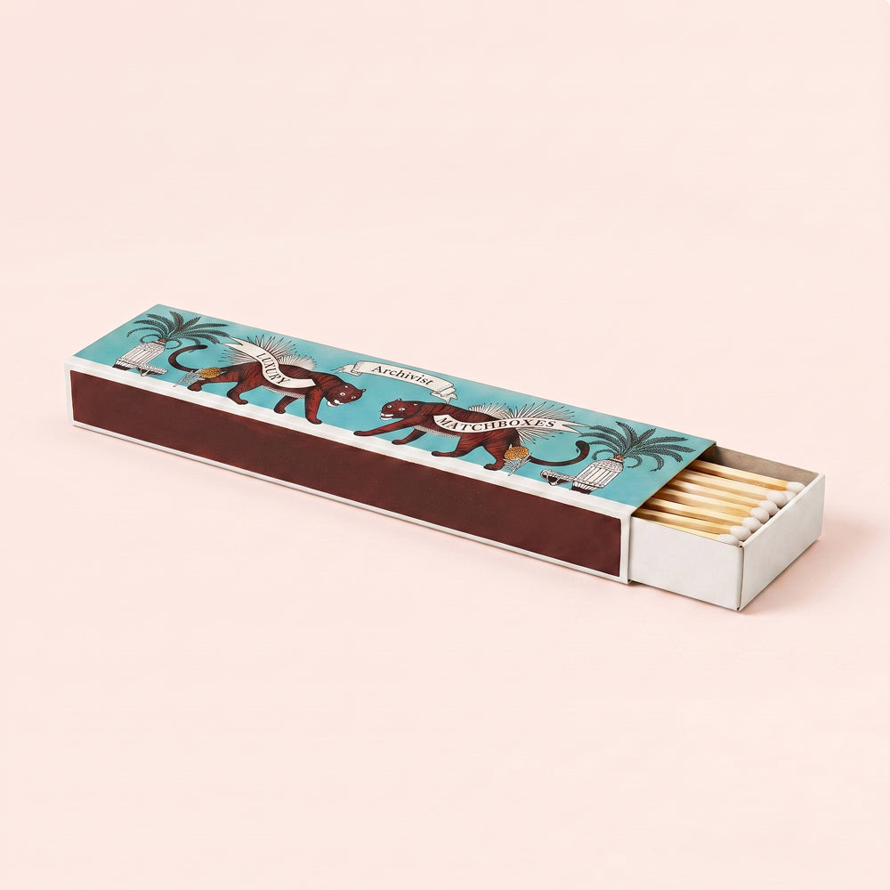 A decorative matchbox with two illustrated tigers and palm trees on a turquoise lid, shown open with matches inside on a light background. Design by Archivist Gallery. Available at Wildschut Antiques & Decor.