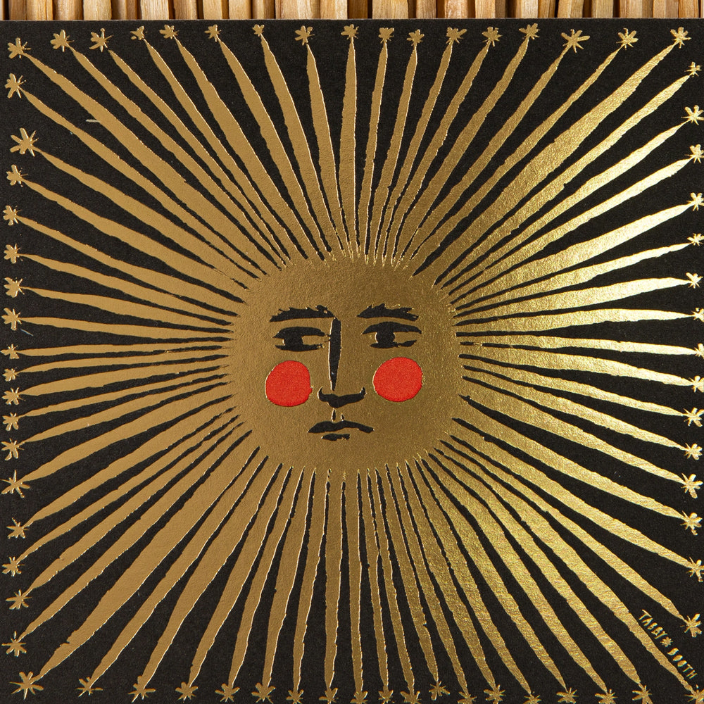 Decorative illustration of a golden sun design featuring a face and red circles on a black background.