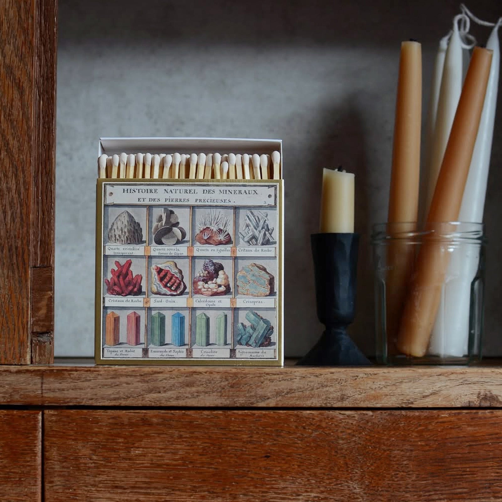 Matchbox with mineral illustrations on a wooden surface with candles in the background