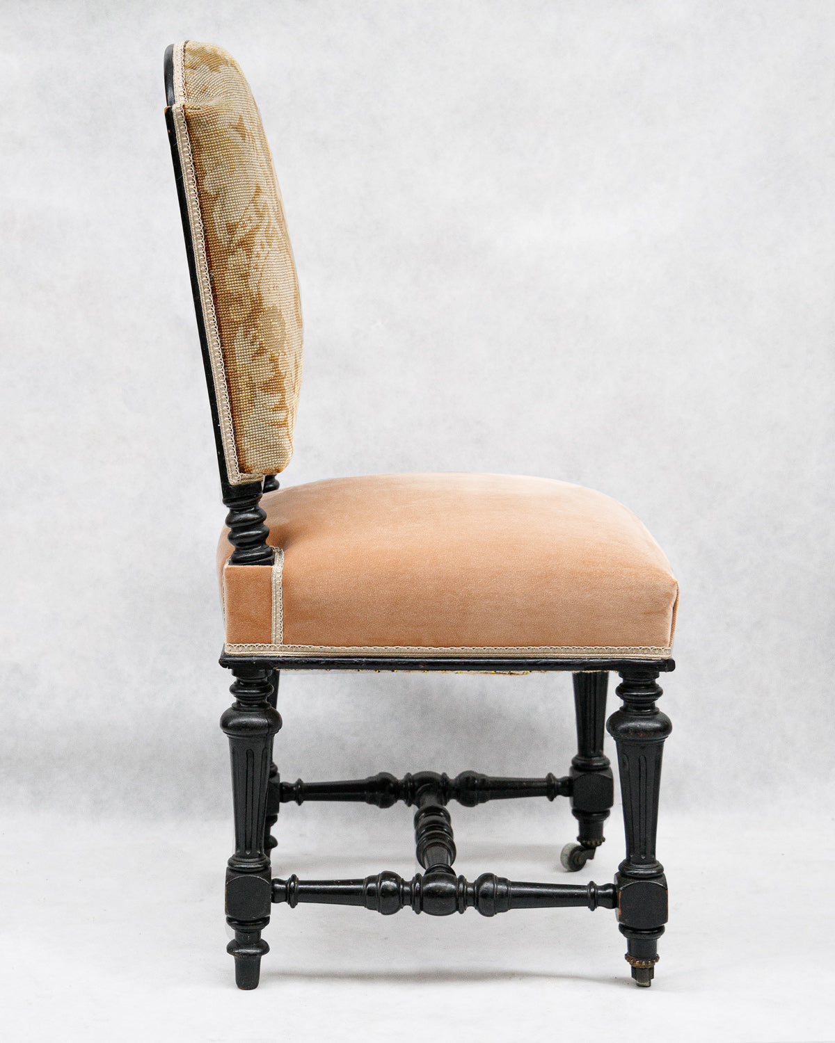 Sideview of an antique chair with a black carved wooden frame, pink velvet seat, and 17th-century style tapestry back