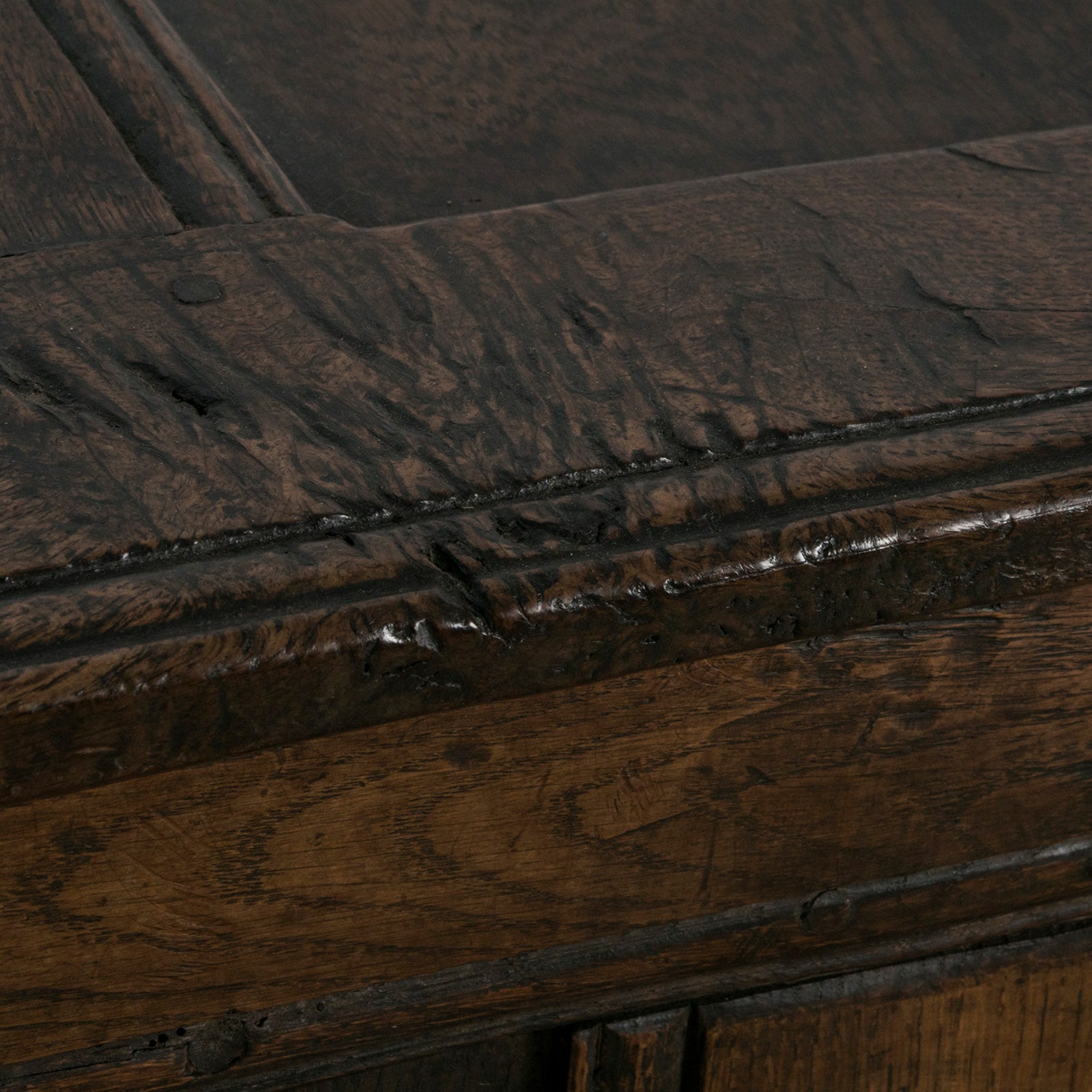 Detail of an antique early 18th-century solid oak chest or coffer, paneled and carved in warm brown tones.
