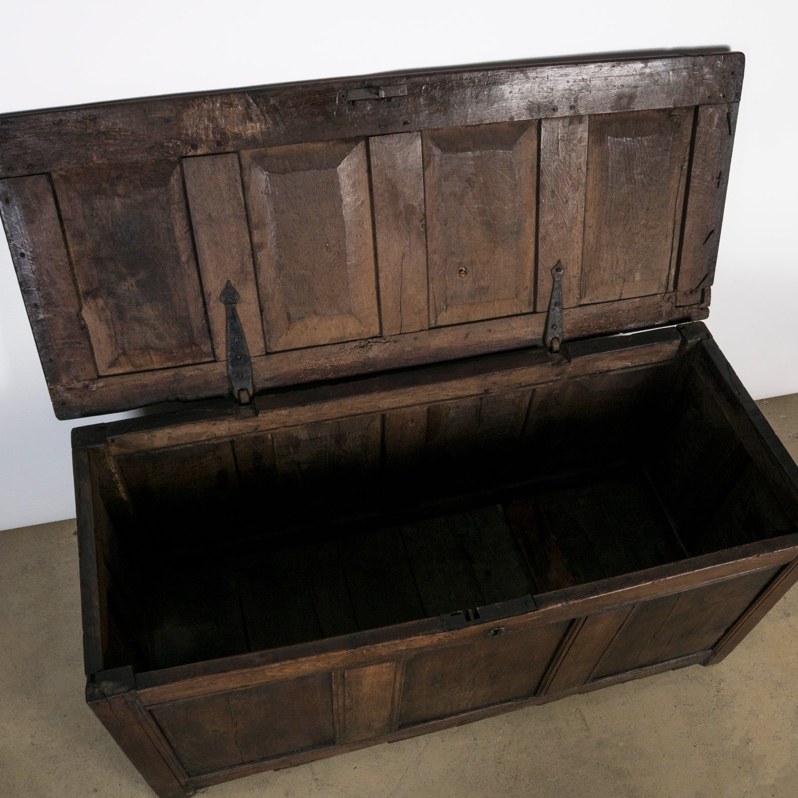 Interior view of an antique early 18th-century solid oak chest or coffer, paneled and carved in warm brown tones.