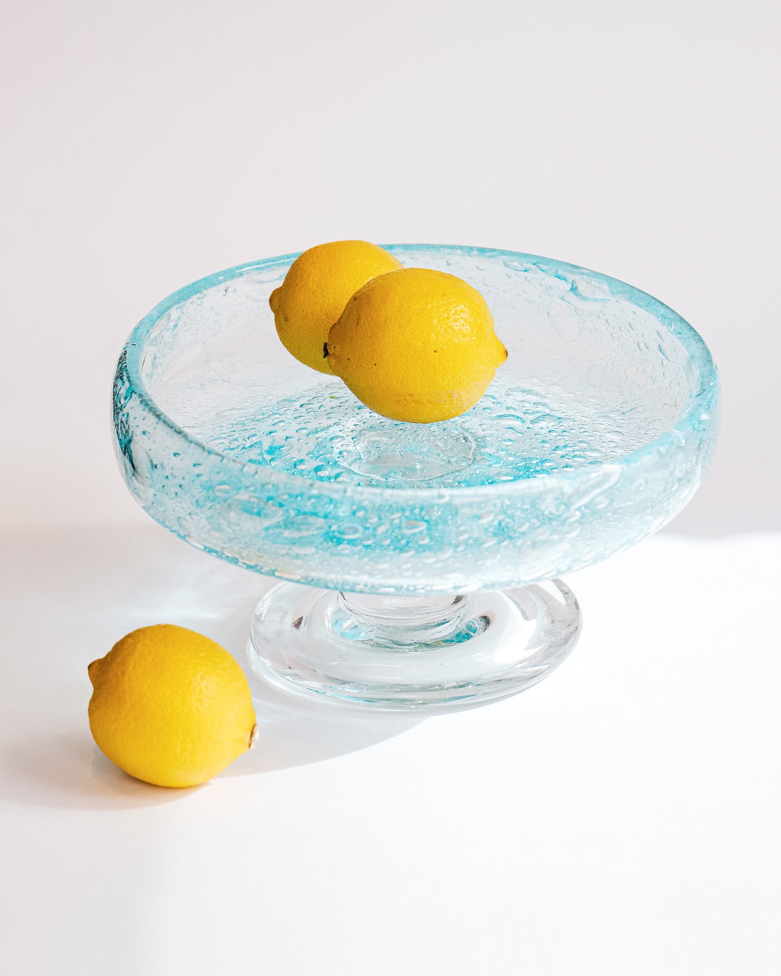 Vintage round blue glass fruit bowl resembling a heavy glass droplet, likely by Biot, France, displayed with three lemons