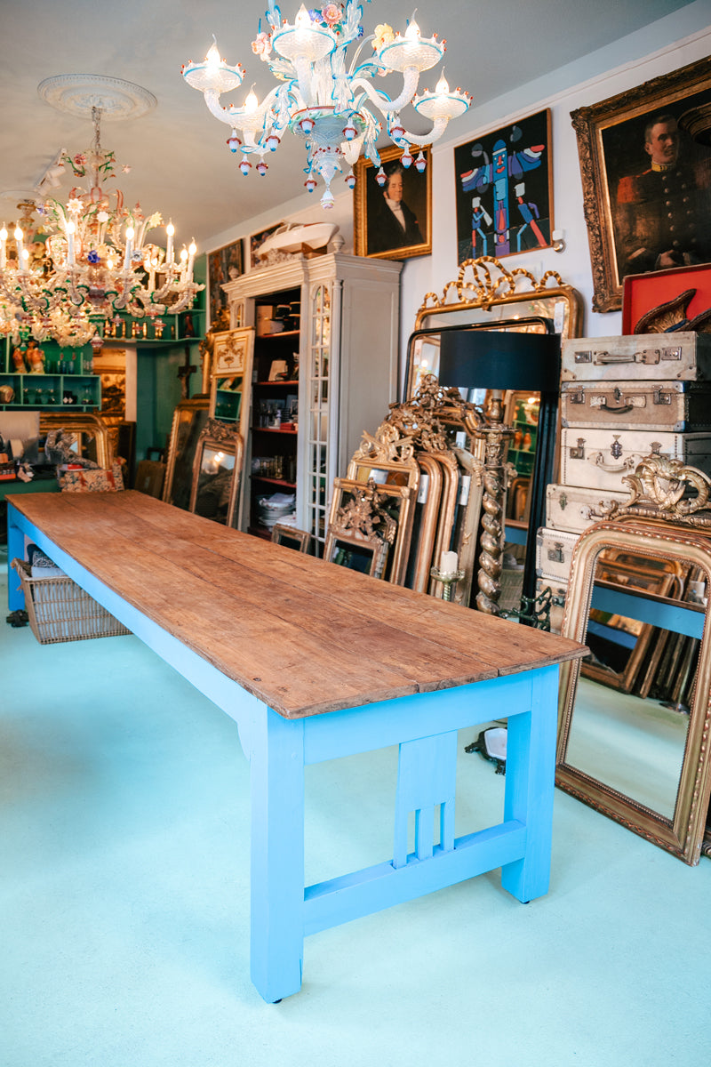 The interior of the Wildschut Antiques store in Amsterdam featuring antique French giltwood mirrors, a long wooden table, several Venetian chandelier, antique portrait paintings and an armoire.