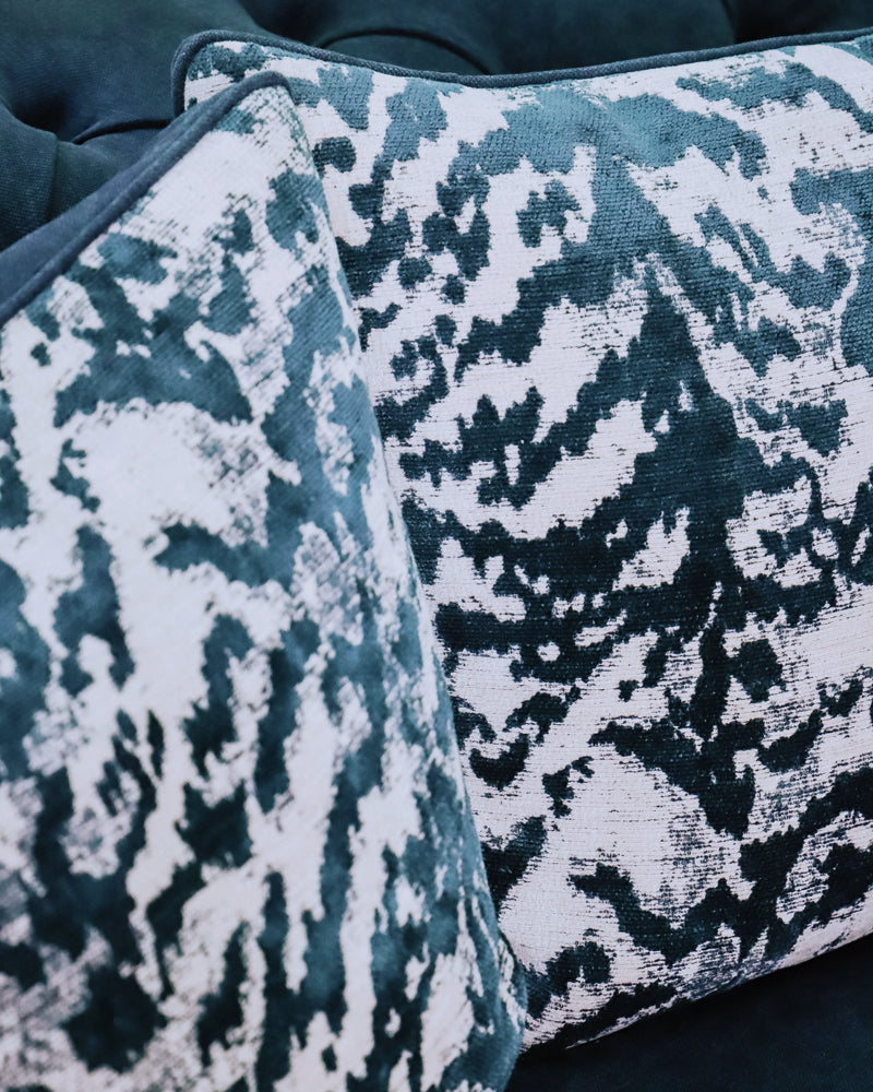 Close-up of a set of two square-shaped throw pillows with a velvet blue tiger pattern on a blue sofa