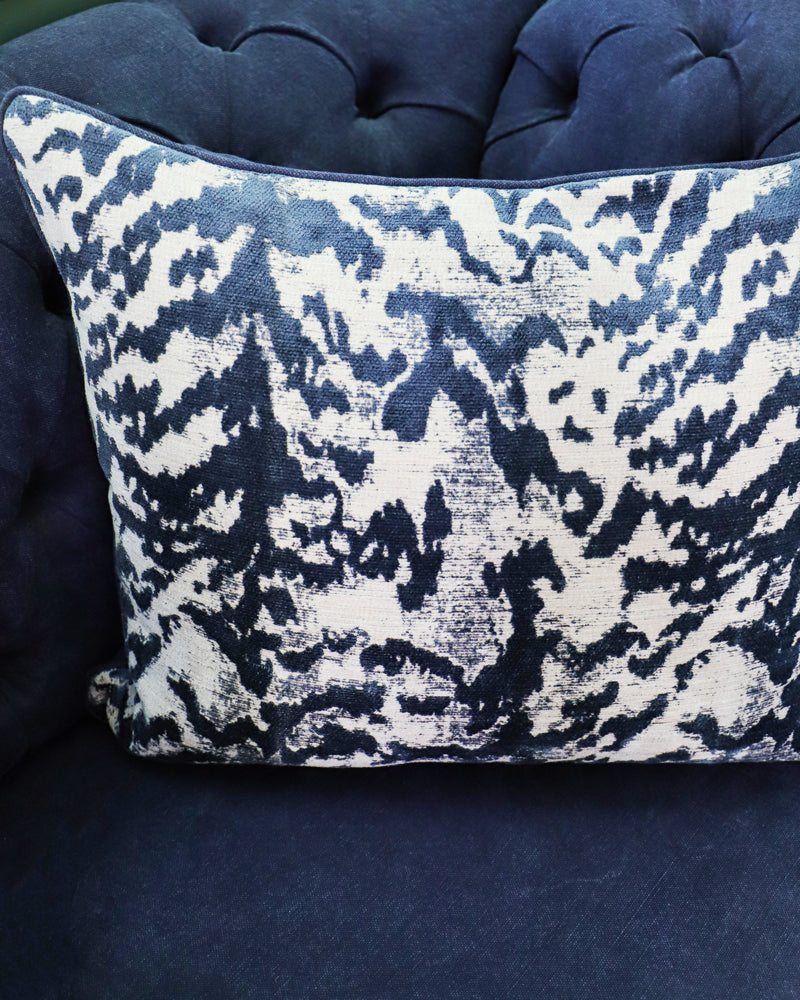 A square-shaped throw pillow with a blue tiger pattern on a silk velvet surface and a natural blue stone-washed linen back on a blue sofa
