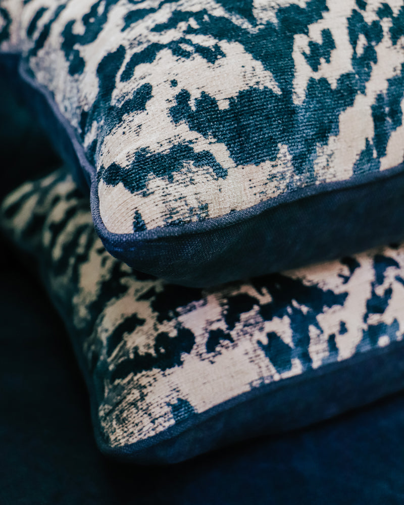 Close-up of a set of two square-shaped throw pillows with a velvet blue tiger pattern on a blue sofa