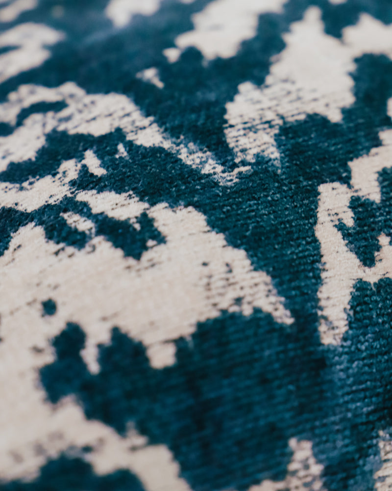 Close-up of a square-shaped throw pillow with a blue tiger pattern on a silk velvet surface and a natural blue stone-washed linen back
